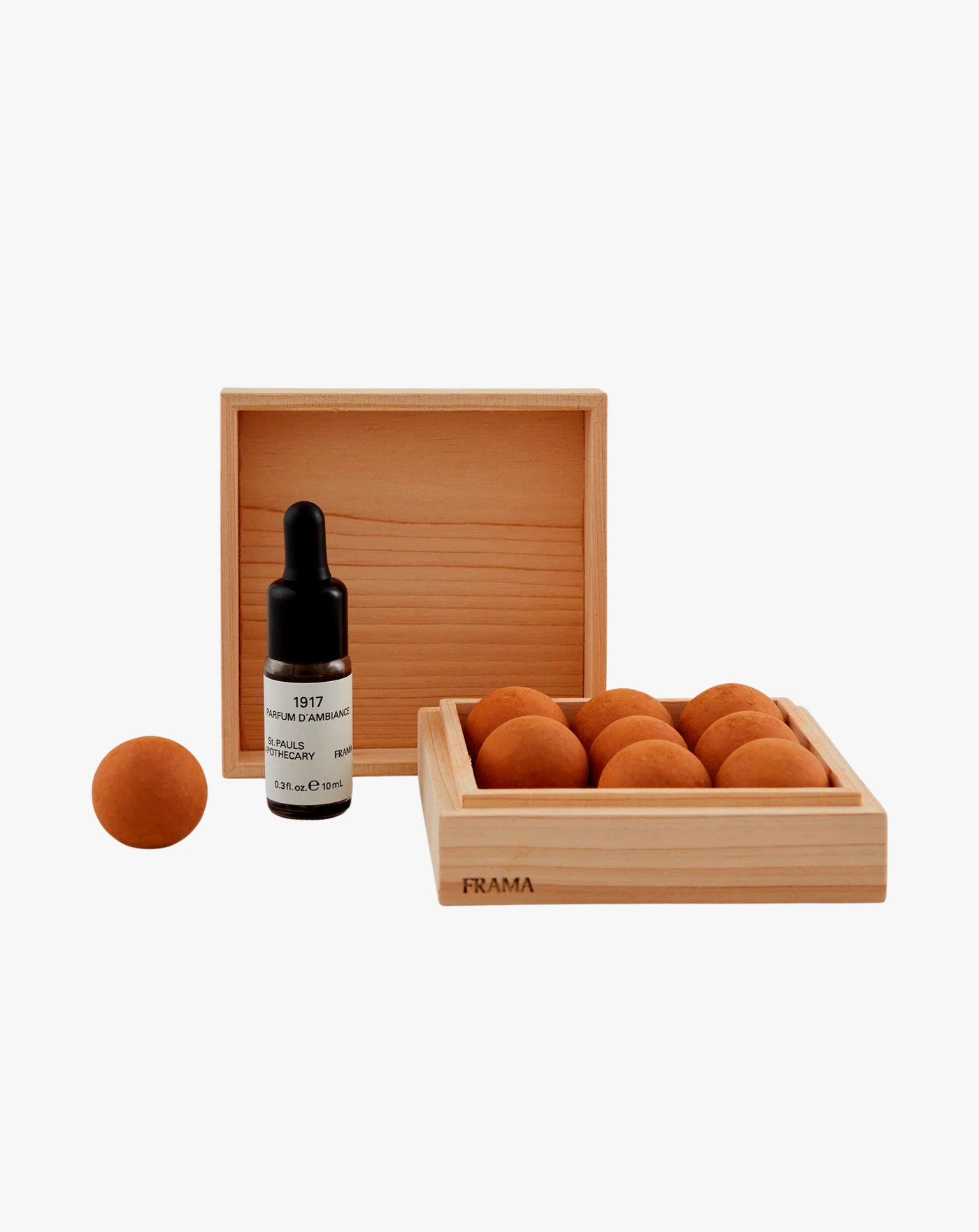 A set of small wooden boxes, one with several brown clay balls and the other holding one brown clay ball and a brown dropper bottle labeled "1917 TUNGA FRAMA". The boxes are simple and elegant, made of light-colored wood.