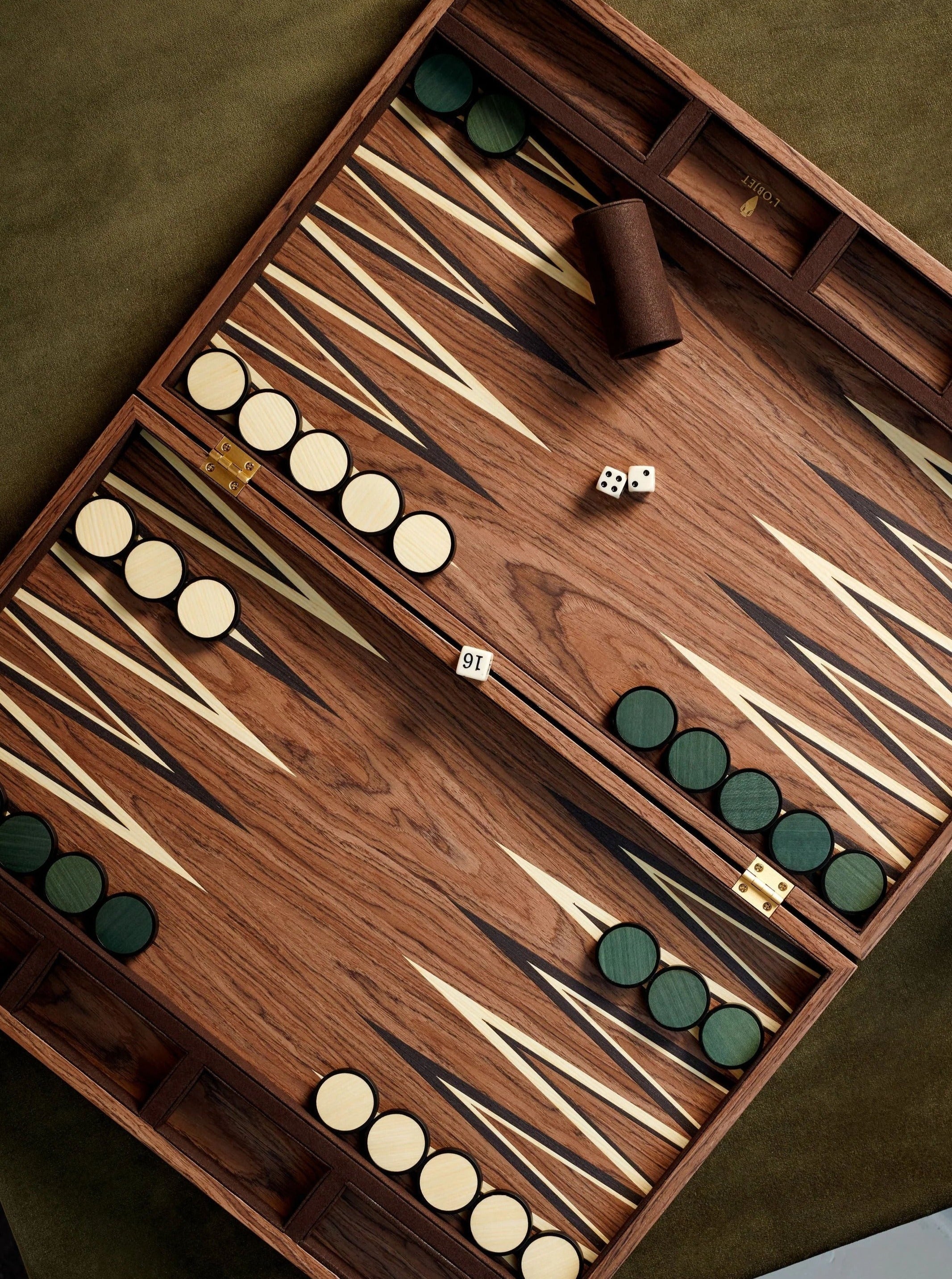 A wooden Luxury backgammon board with light and dark triangular patterns. The game pieces are divided into two colors: light and dark green, arranged in starting positions. Two dice and a dice cup are placed on the board.