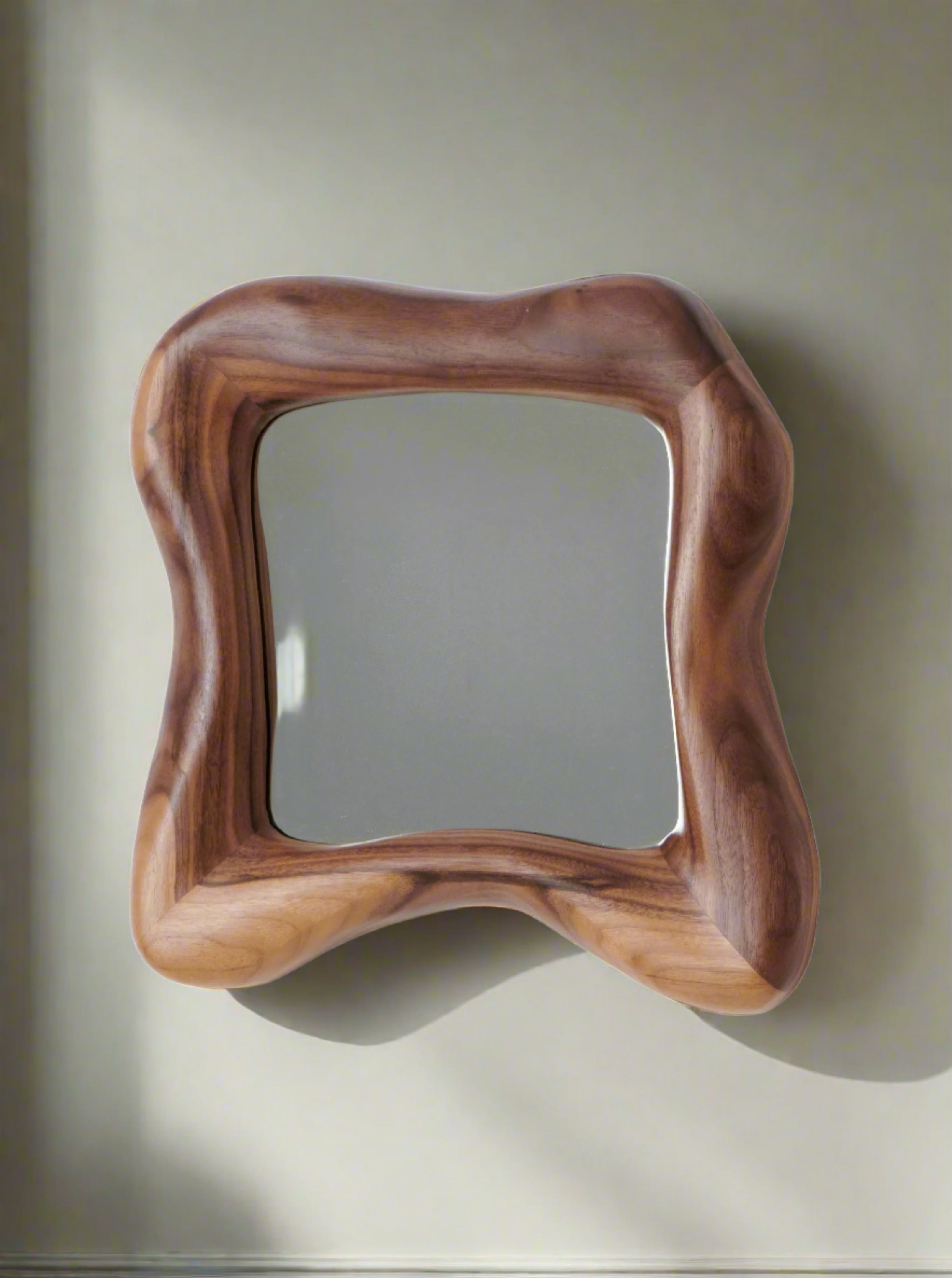 A square mirror with a wavy wooden frame featuring natural, smooth curves, hangs on a plain wall. The frame’s rich wood grain adds a warm, organic touch to the minimalist setting.