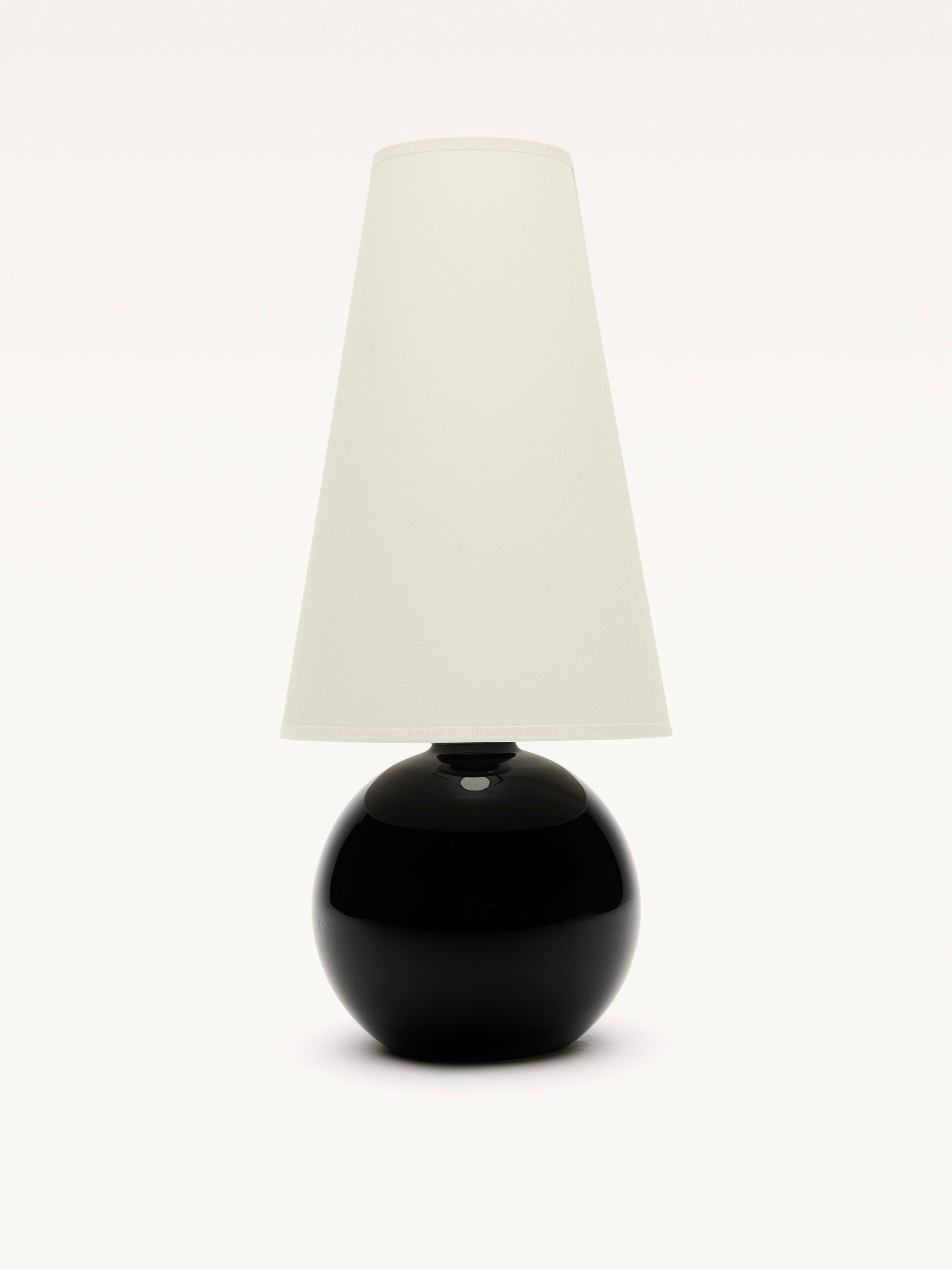 The Large Black Opalin Glass Lamp by Galerie MLS has a sleek black spherical base and a tall white cylindrical shade. A subtle brass ring adds to its modern design, making it a striking centerpiece against a white background.