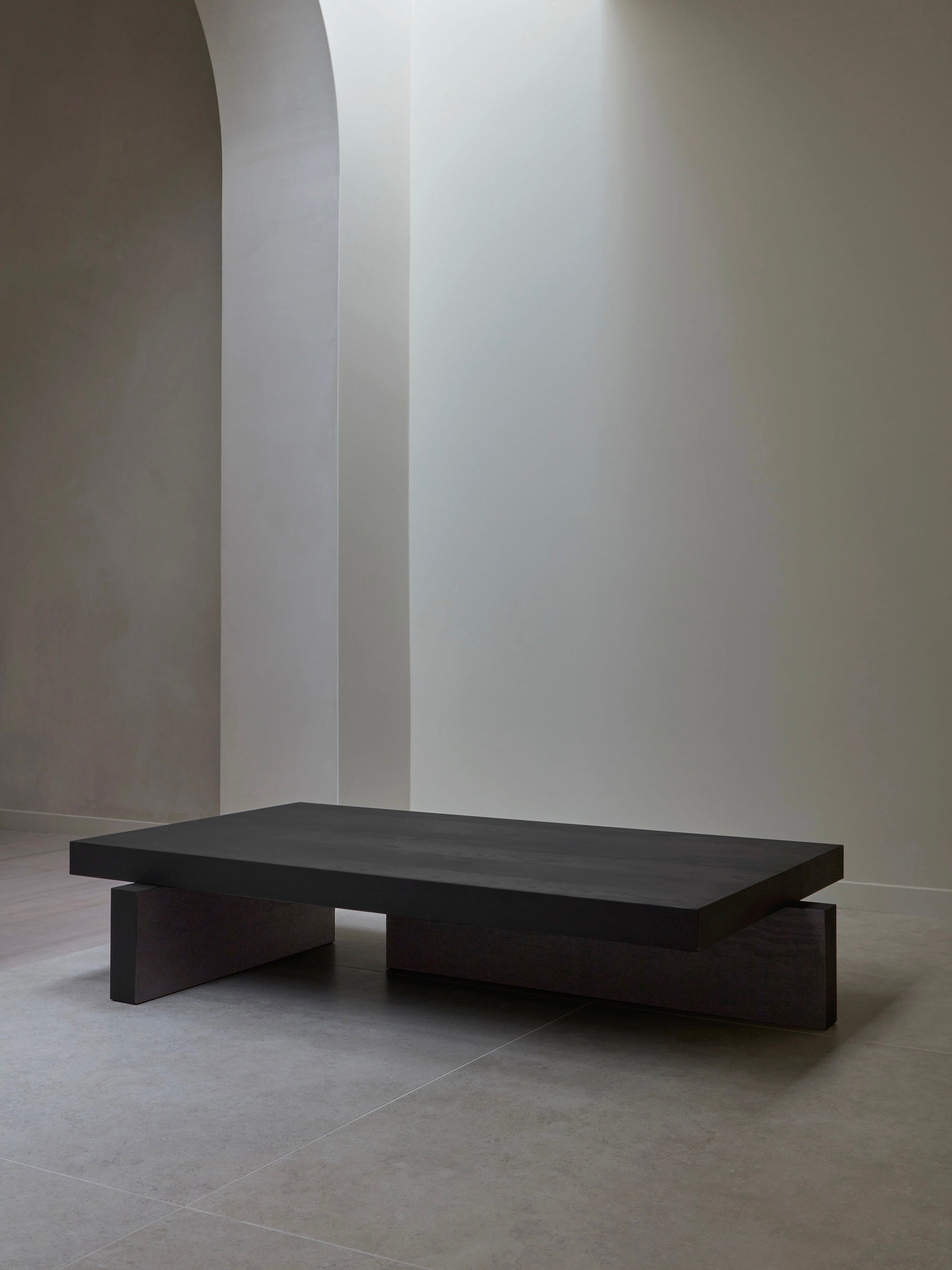 A minimalist room showcases the Mokko Hari Coffee Table, featuring a low, dark rectangular design with geometric patterns and solid wood parts. Set against a light wall with a large archway, the customizable table contrasts beautifully with its bright surroundings.