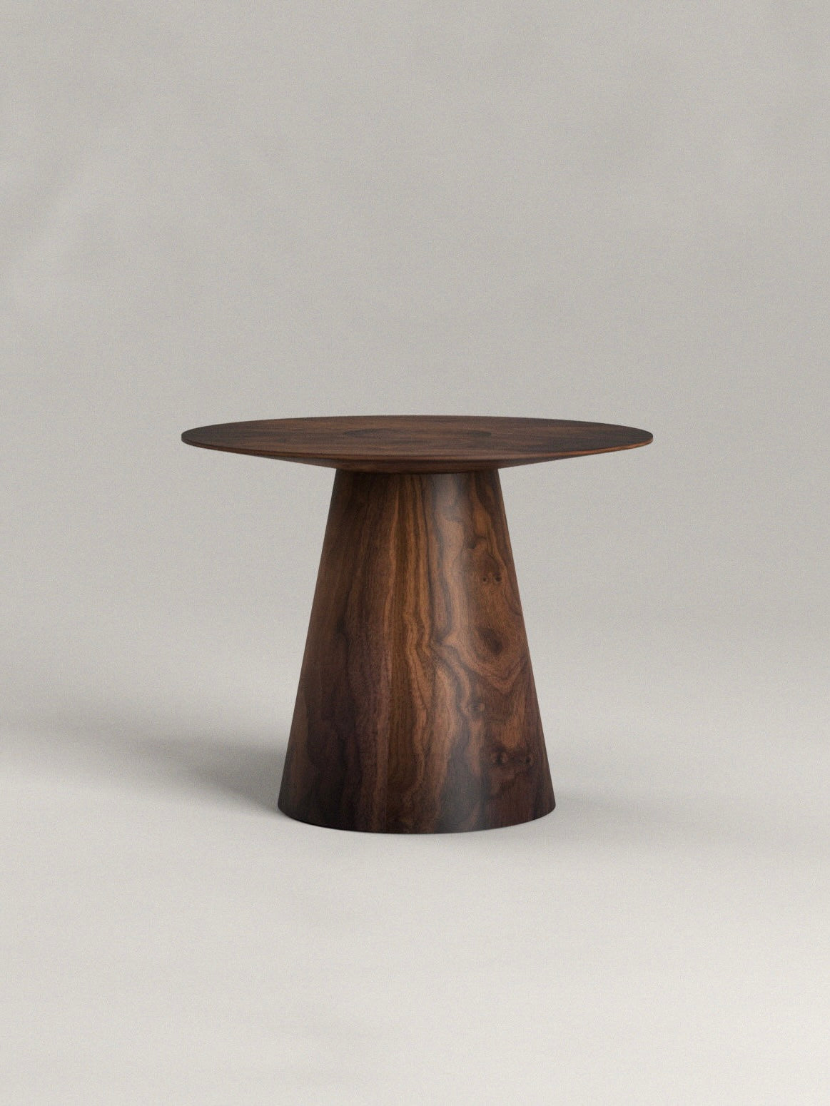 The Totem Side Table by Siete Studio stands against a plain gray background, featuring a small, round surface handcrafted from walnut with striking natural wood grain patterns on its conical base.