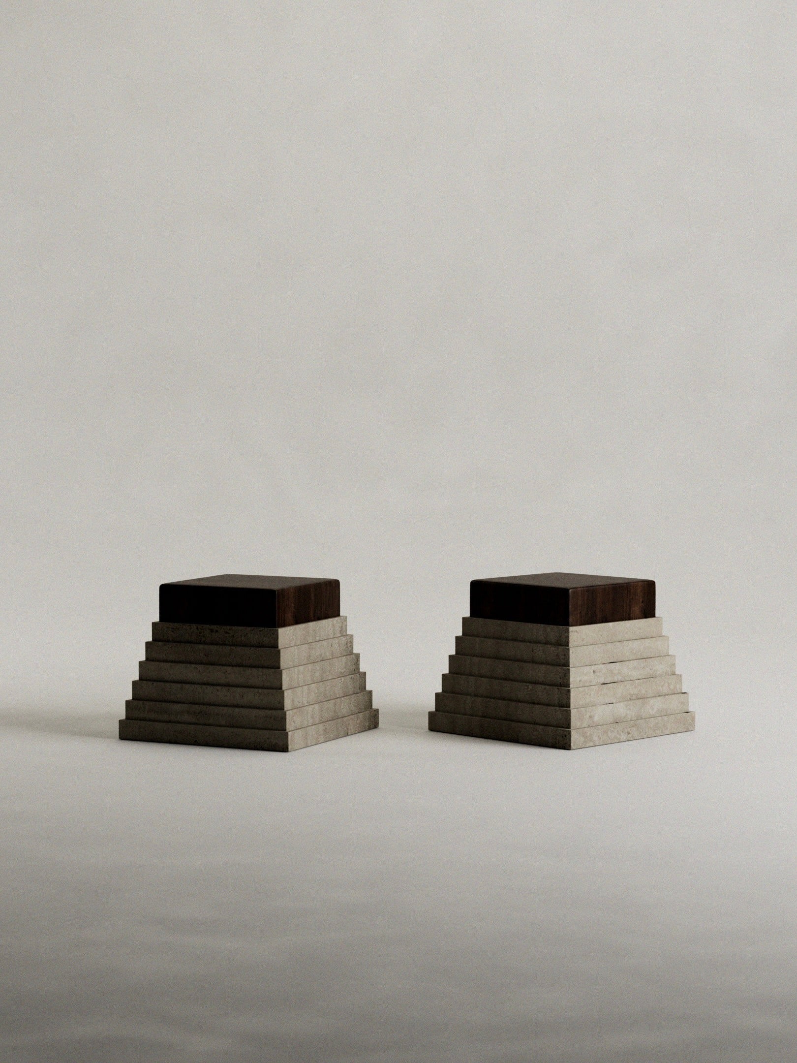 Against a neutral backdrop, two pyramid-shaped 'Calakmul' side tables by Siete Studio stand side by side. They boast solid walnut tops with handcrafted travertine bases in a minimalistic, symmetrical design featuring tiered, rectangular layers.