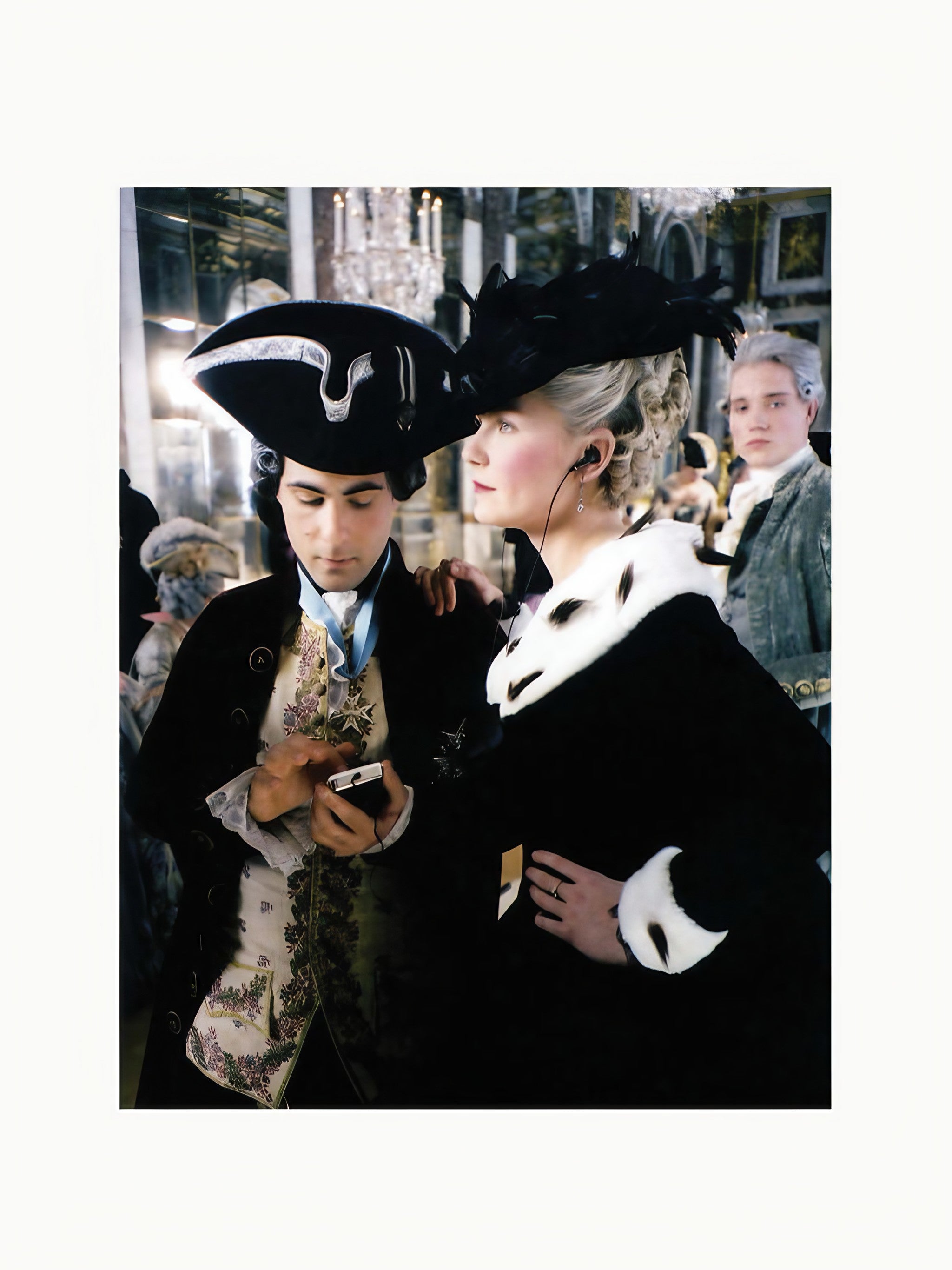 A historical reenactment scene depicting two individuals in 18th-century attire, one holding a Archive Sofia Coppola mask inspired by "Lost in Translation" and the other a small bouquet, surrounded by other costumed Maison Plage.