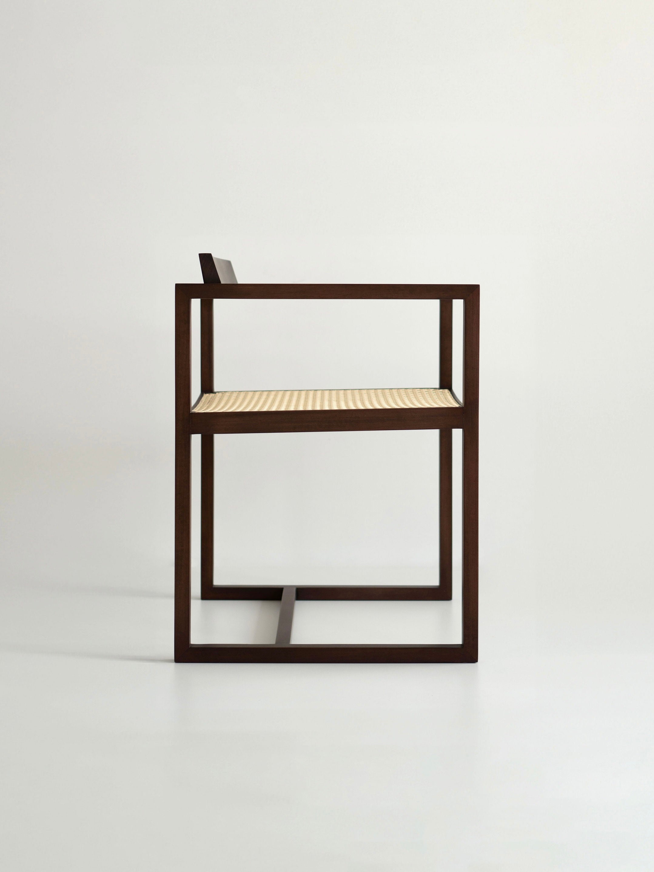 The "Amélia" Armchair by Andre Grippi features a modern, minimalist design with a dark wooden frame and a light woven straw seat, shown in profile against a plain white background.