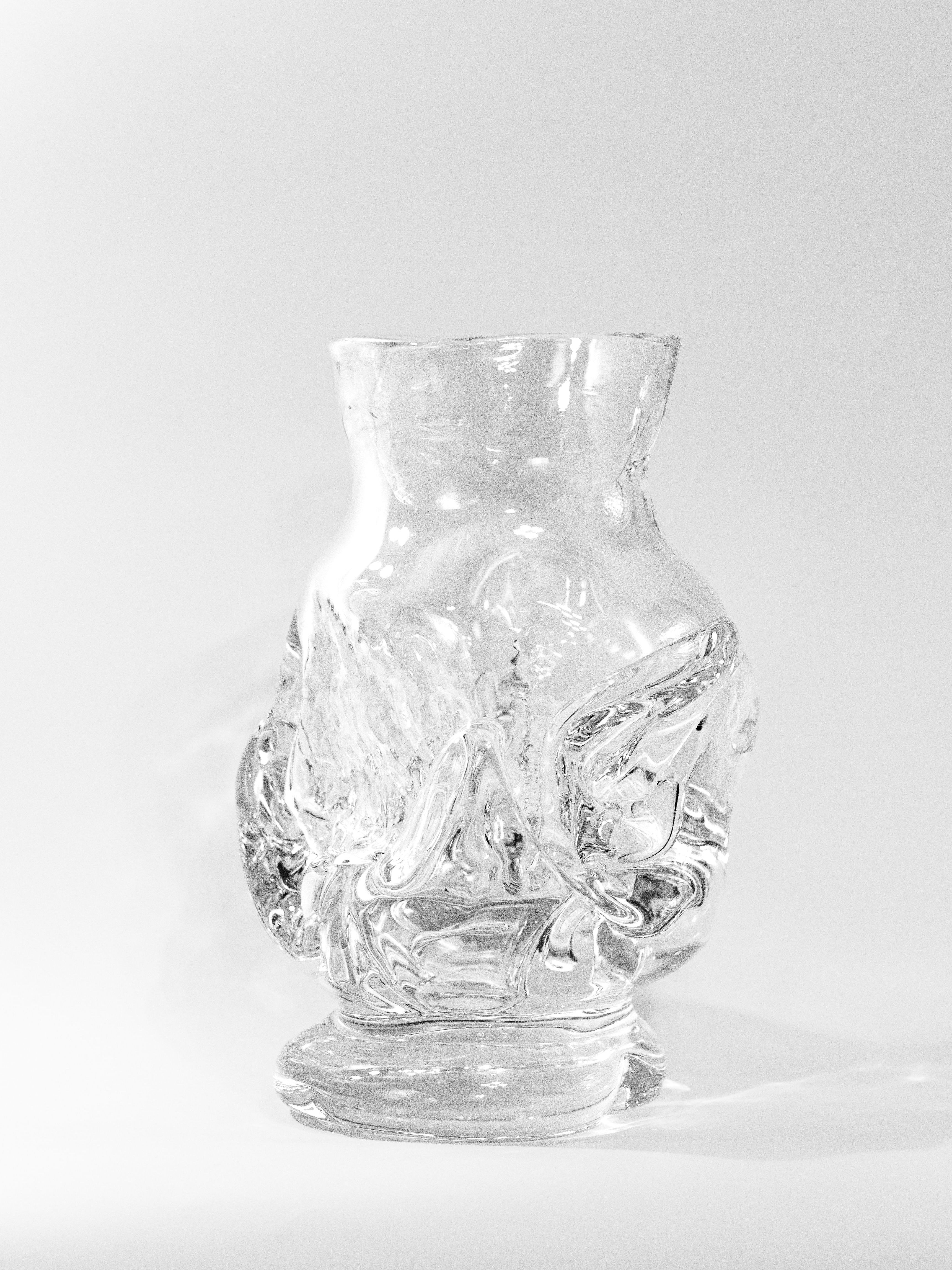 The Free Blown Vase by SzkĆo Studio, crafted from transparent lead-free glass, stands against a white background. Its glossy finish and swirling patterns reflect light elegantly, showcasing its sophisticated appearance.