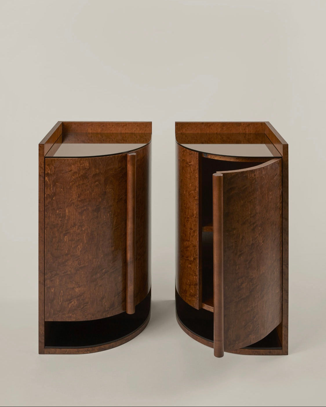 Two Yves Bar / Bedsides Tables by HAUVETTE & MADANI, featuring a rich, dark brown finish and shaped like half-moons, are positioned side by side as elegant bedside tables. The left table remains closed, while the right one is slightly open to reveal its inner shelving. The design showcases sleek, minimalist lines complemented by a mirrored top.