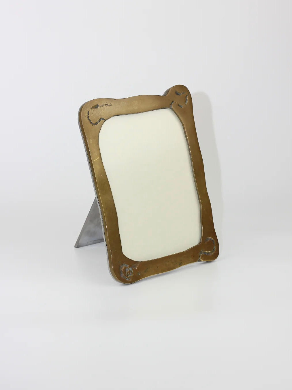 The Brutalist Mirror by Boga Avante Shop is a vintage piece with a brass border and ornate corners. It stands upright, its industrial finish highlighting an empty space for your photo or artwork, embodying minimalist design.