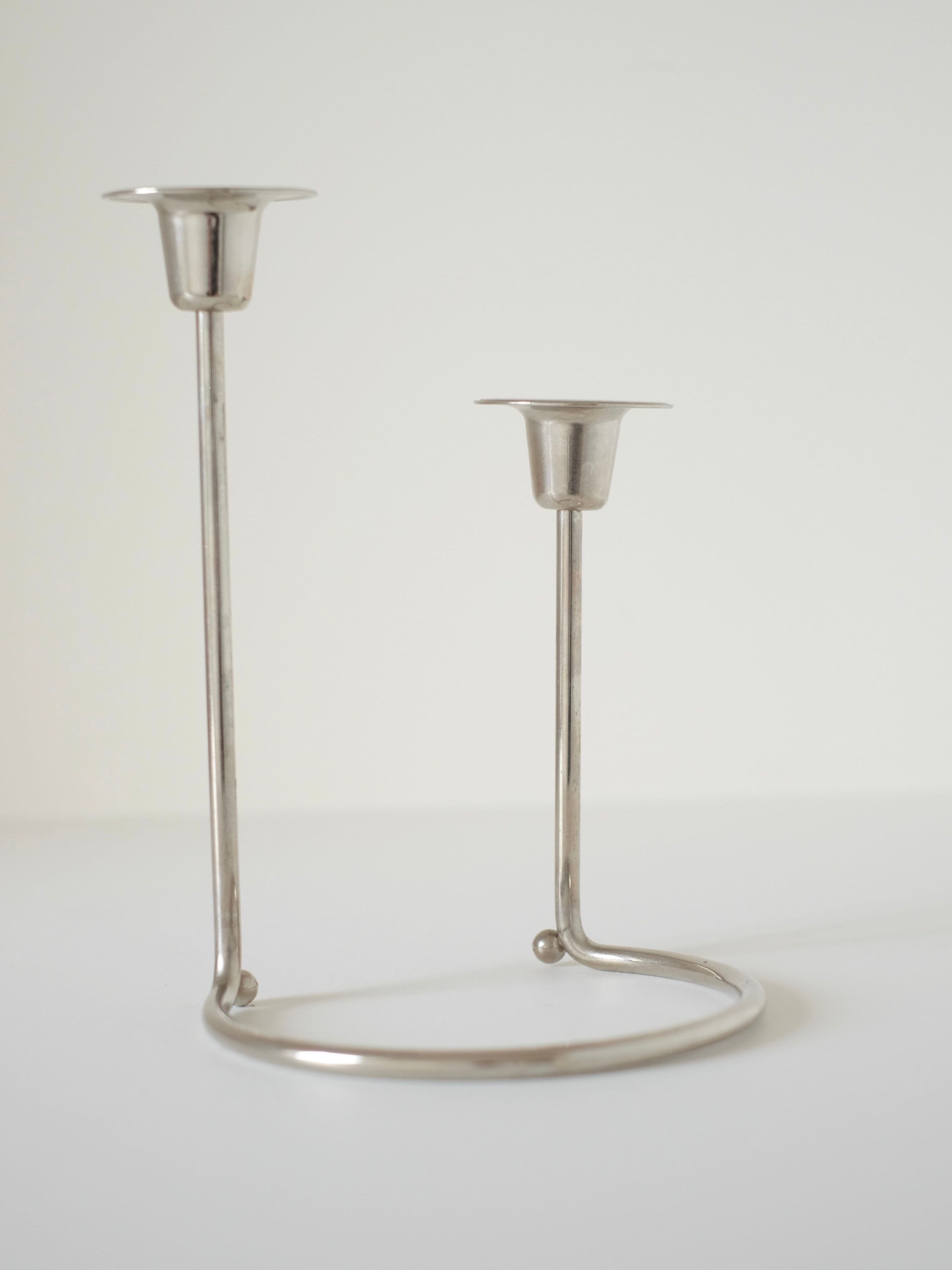 The Silver WMF Candle Holder by septembre studios features a minimalist design with two arms of differing heights on a circular base, echoing the classic style of a vintage 70’s WMF piece, photographed against a plain white background.