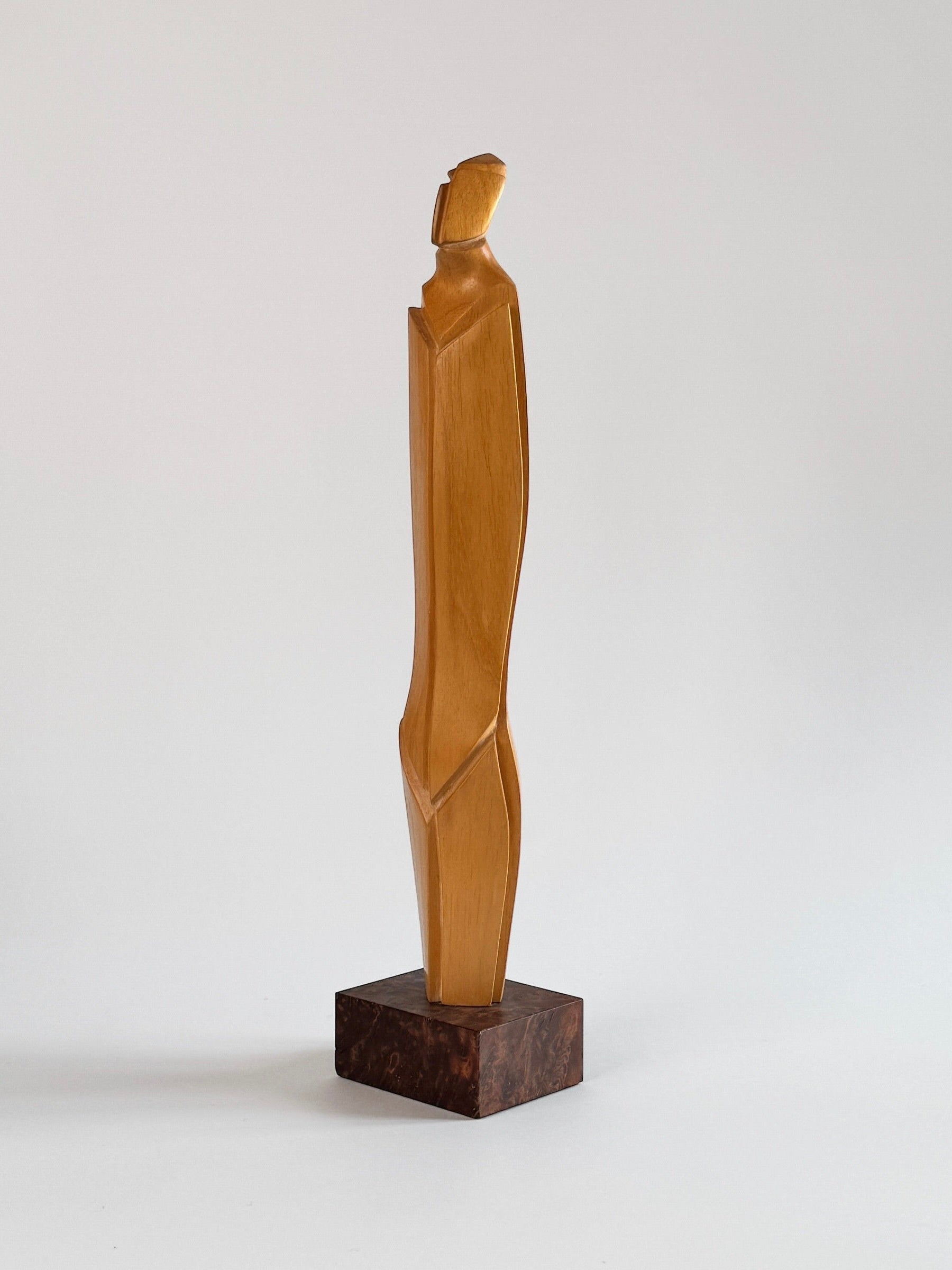 Crafted by Figuresdesign, this Light Wood Sculpture by Pierre Dedieu showcases a tall, abstract human form with simplified geometric lines and a smooth finish. It stands elegantly on a dark square base, set against a plain background.