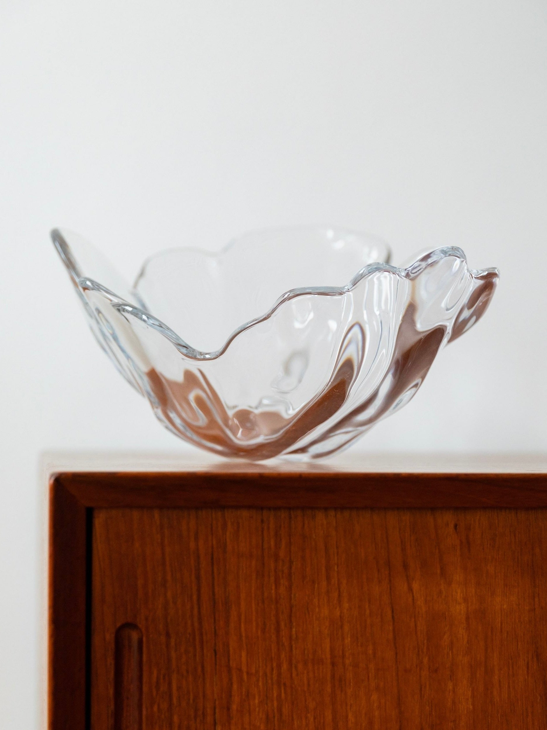 The XL Danish Vintage Crystal Glass Bowl by Lütken, offered by Bottega Jacobs, with its distinctive clear, wavy-edged design and vintage charm, sits atop a wooden cabinet against a plain white background.