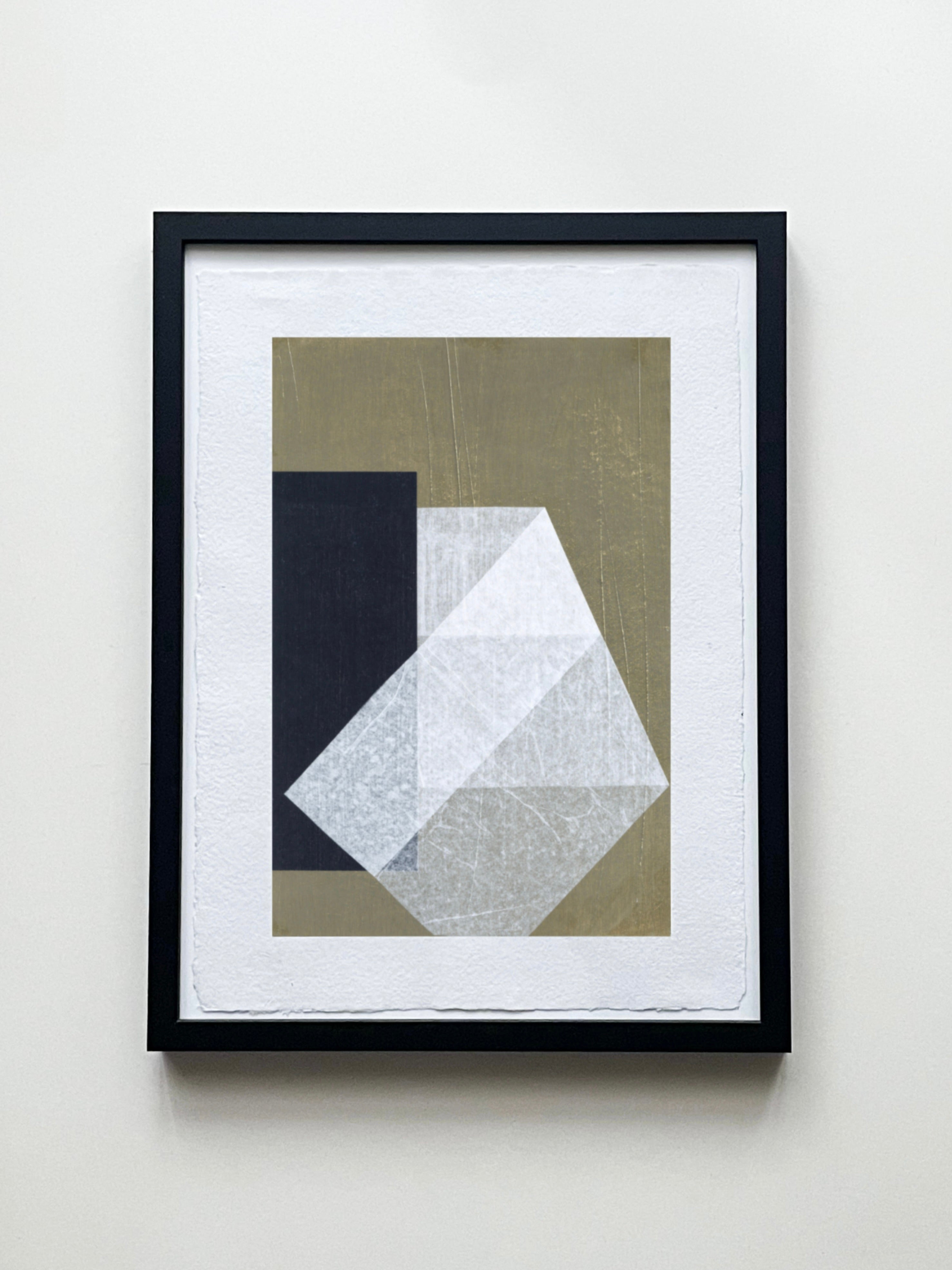 The "Stone and Gap No.06" Art Paper Collage by Julita Elbe showcases overlapping geometric shapes in white, gray, and black on a muted green backdrop. It's presented in a slim black frame, creating a layered texture against a light wall.