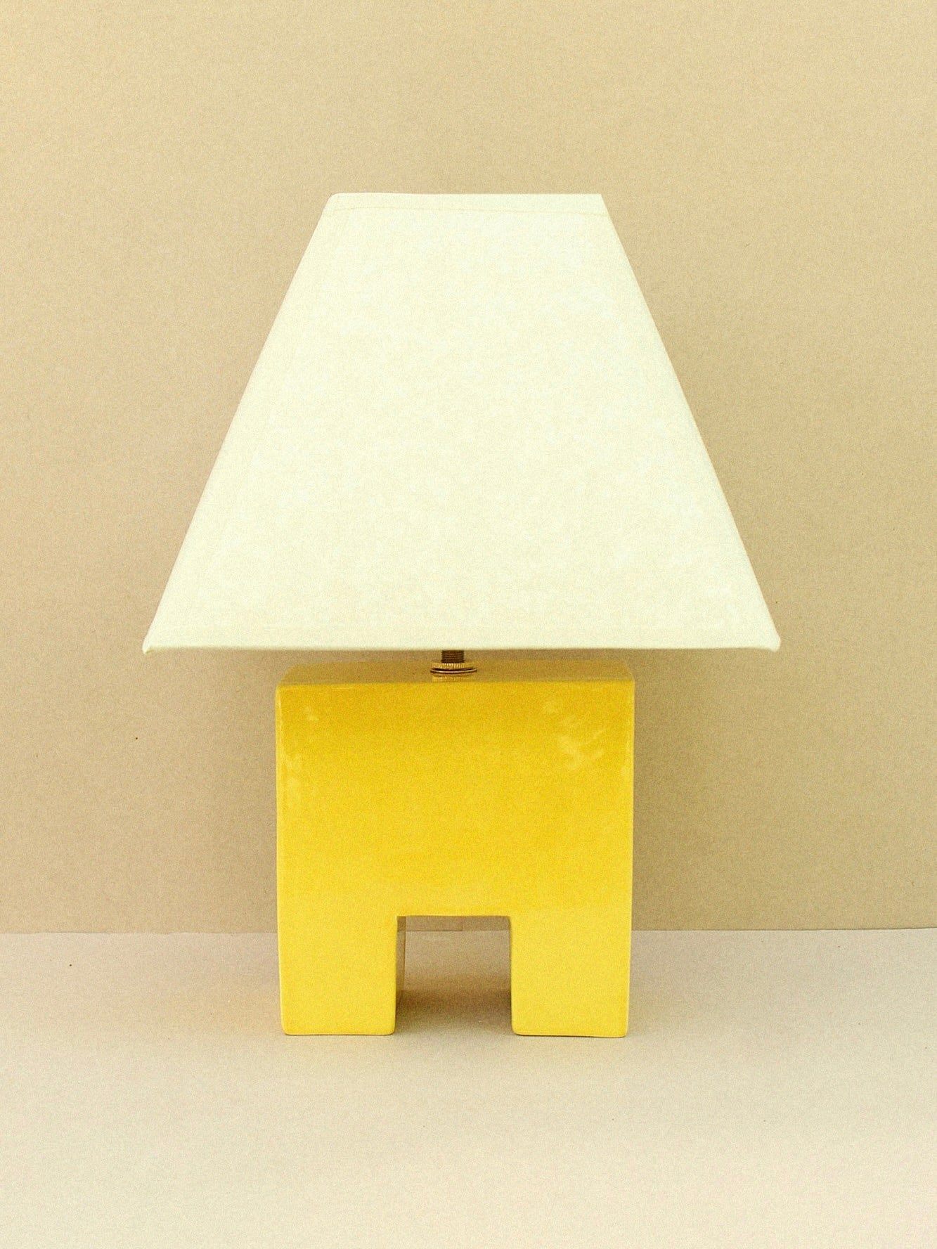 The Cristo Lamp (Sol) by Casa Veronica showcases a glossy yellow geometric ceramic base and a white custom lampshade, set on a neutral surface with a beige background.