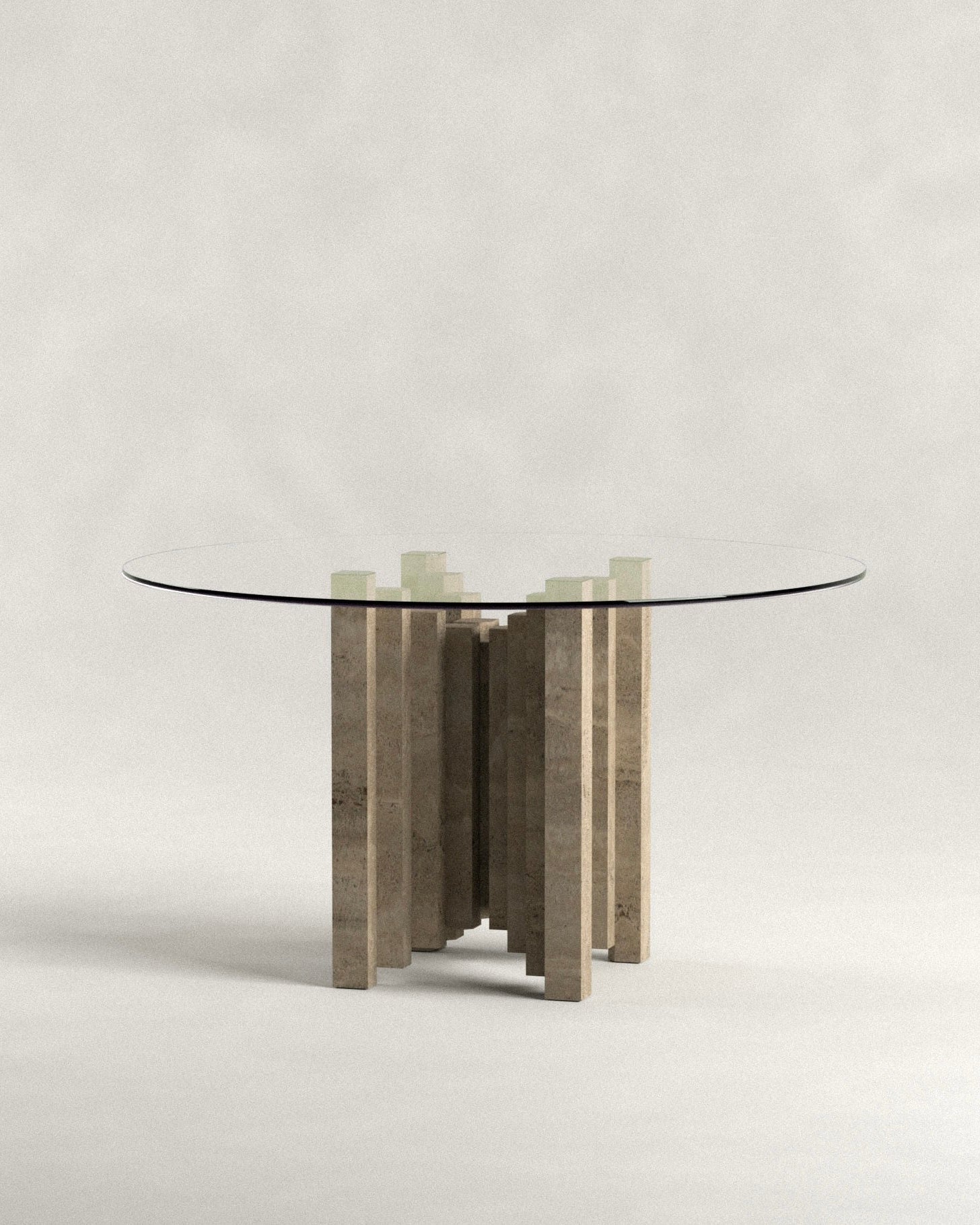 The 'Calakmul' Dining Table S2 by Siete Studio features a modern round glass top supported by a unique travertine base with handcrafted stone pillars arranged circularly. The background is a neutral, light gray, enhancing its elegant design.