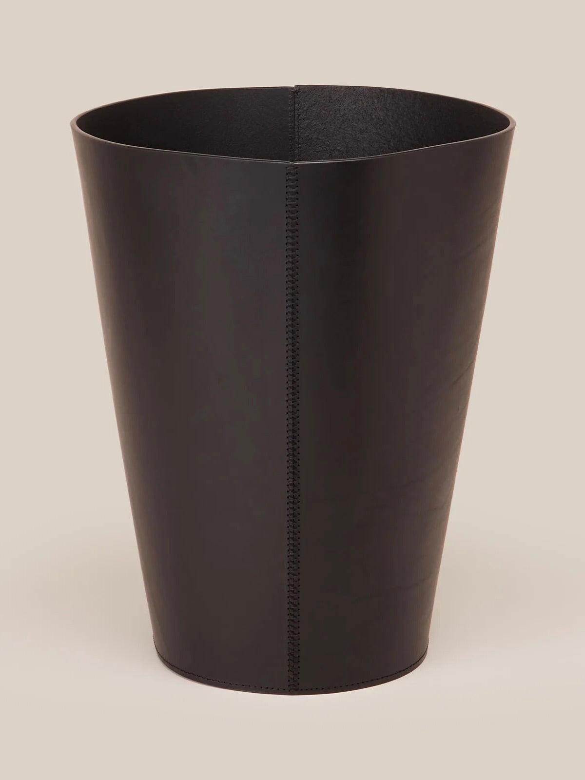 The Leather Wastepaper Bin by Paradise Row is a luxurious piece featuring a smooth leather finish with a distinctive vertical seam, beautifully presented against a simple beige backdrop, showcasing elegant interior design.