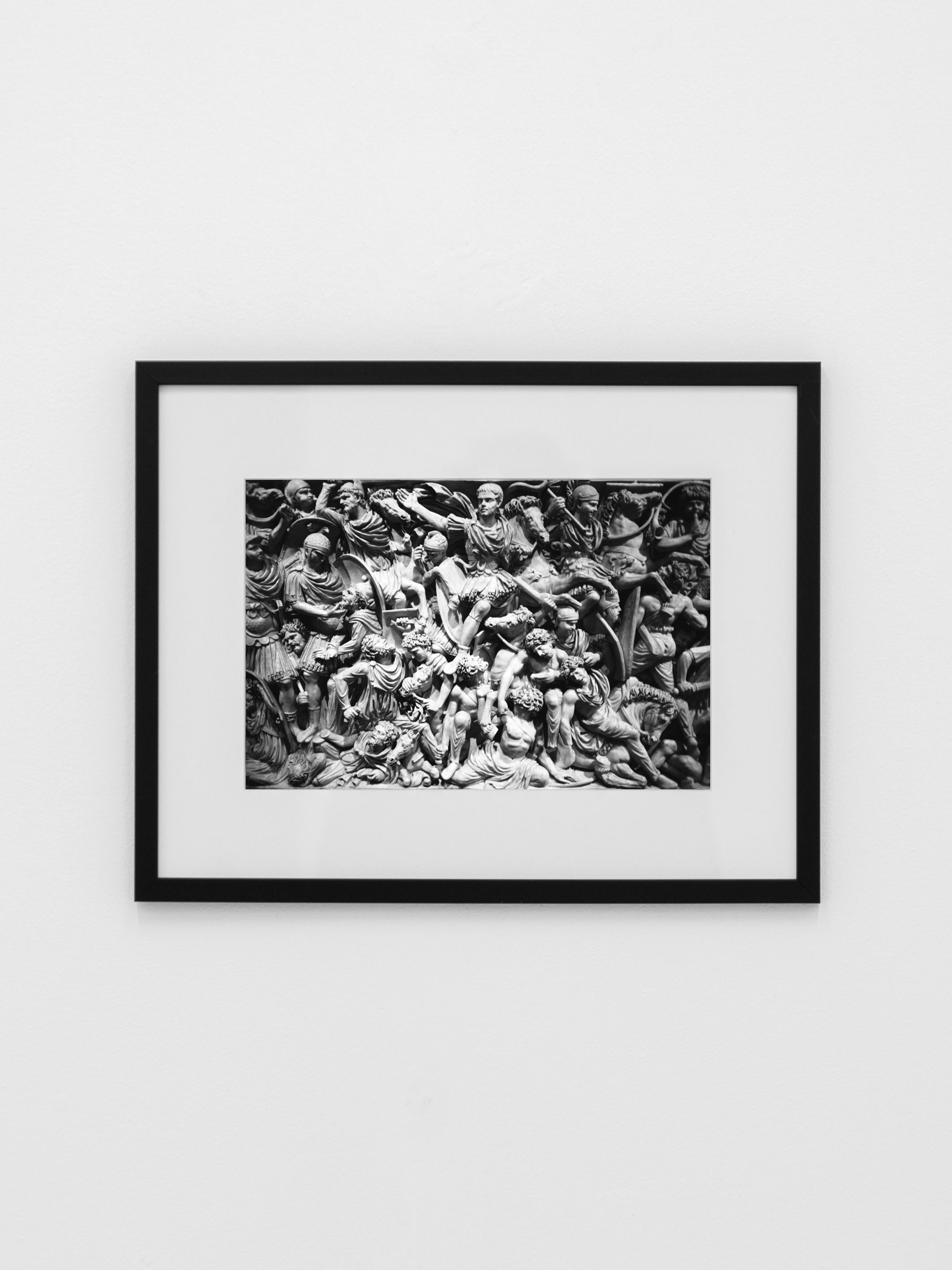 ‘Memory #11’ Photography by COSEINCORSO is a limited edition framed black-and-white print, featuring an intricate stone relief with human figures and detailed carvings, elegantly displayed on a plain white wall.