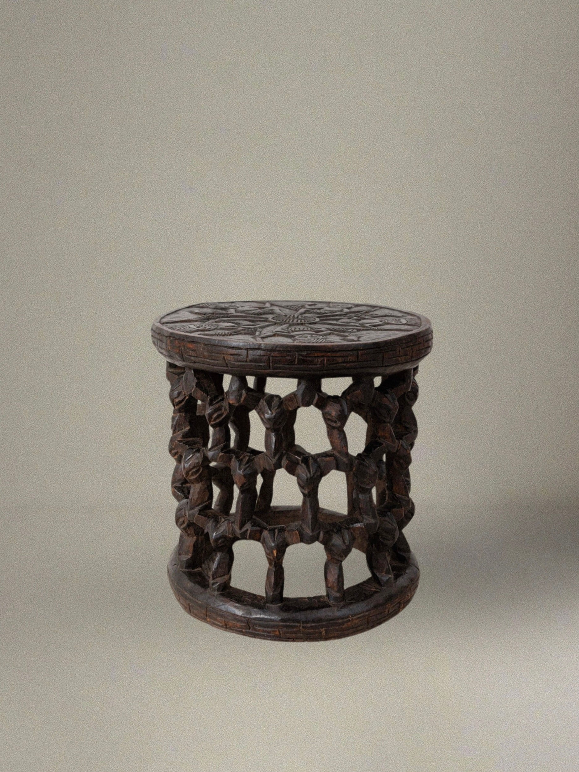 A Hand-Carved Stool from Cameroon 1950s by Bottega Jacobs, featuring a round, intricately carved lattice-like design and a detailed top inspired by African tradition, stands against a neutral background.