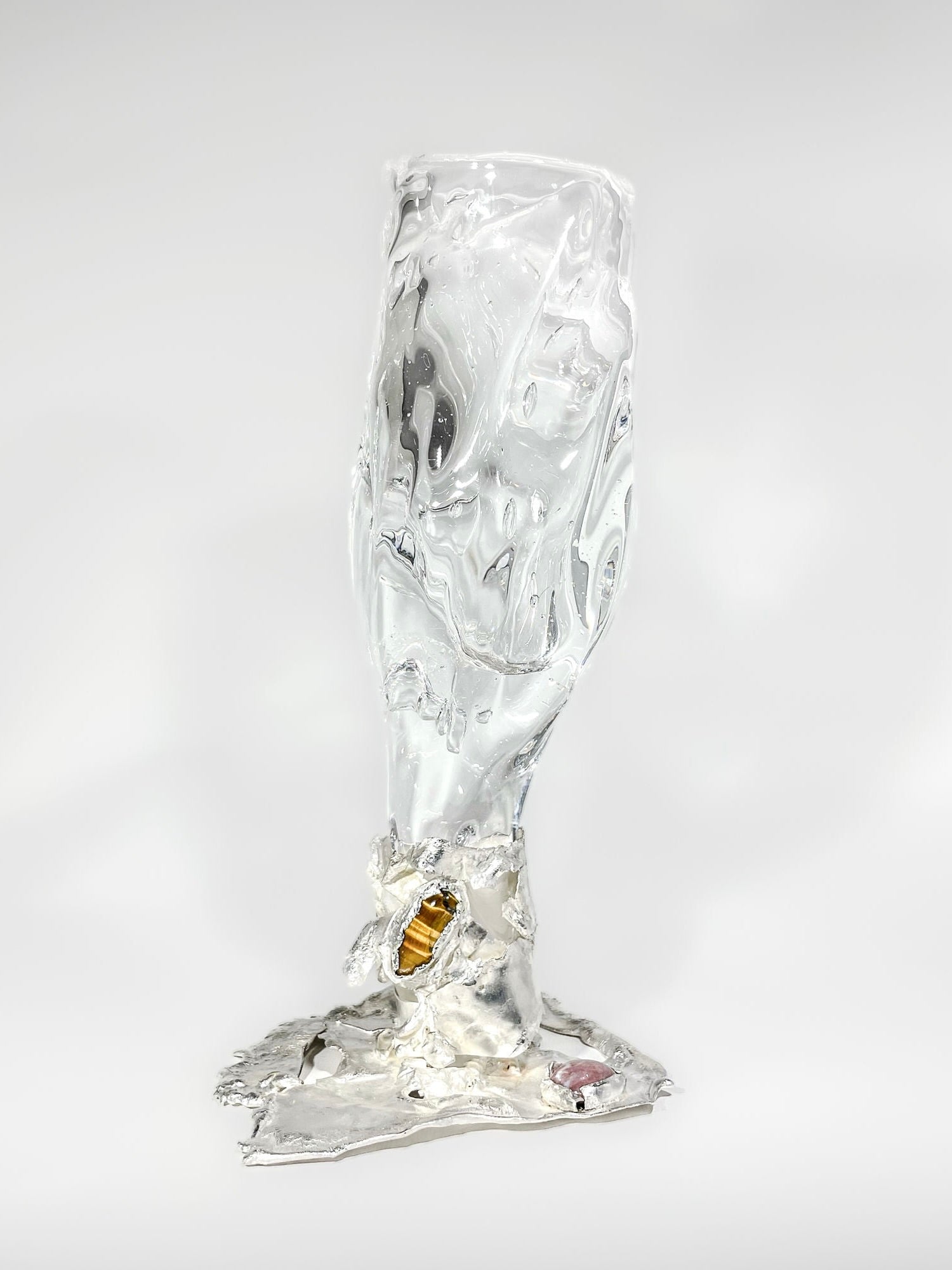 The Jewelled Goblet no. 4 by Lindsey Fontijn from Szkło Studio is a uniquely shaped hand-blown glass sculpture resembling a melting wine glass. It has a distorted, fluid-like appearance and melds into a metallic base with hints of gold and other reflective surfaces, creating a surreal and abstract impression.