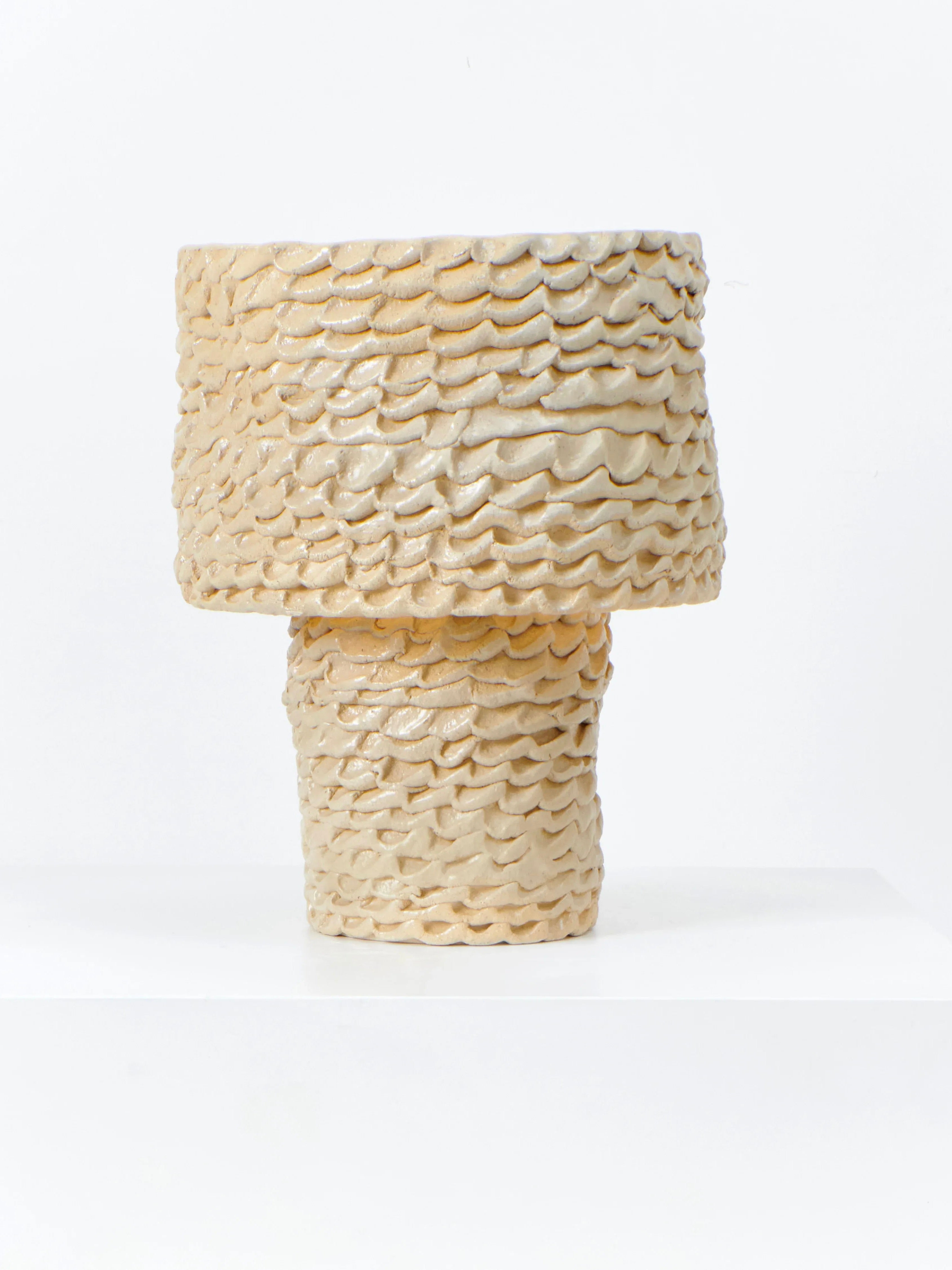 The Casa Table Light (round) by Project 213A features a textured, wavy ceramic surface with a light beige glaze, a wide top, and narrow base, reminiscent of handmade artistry, displayed on a white surface against a plain backdrop.