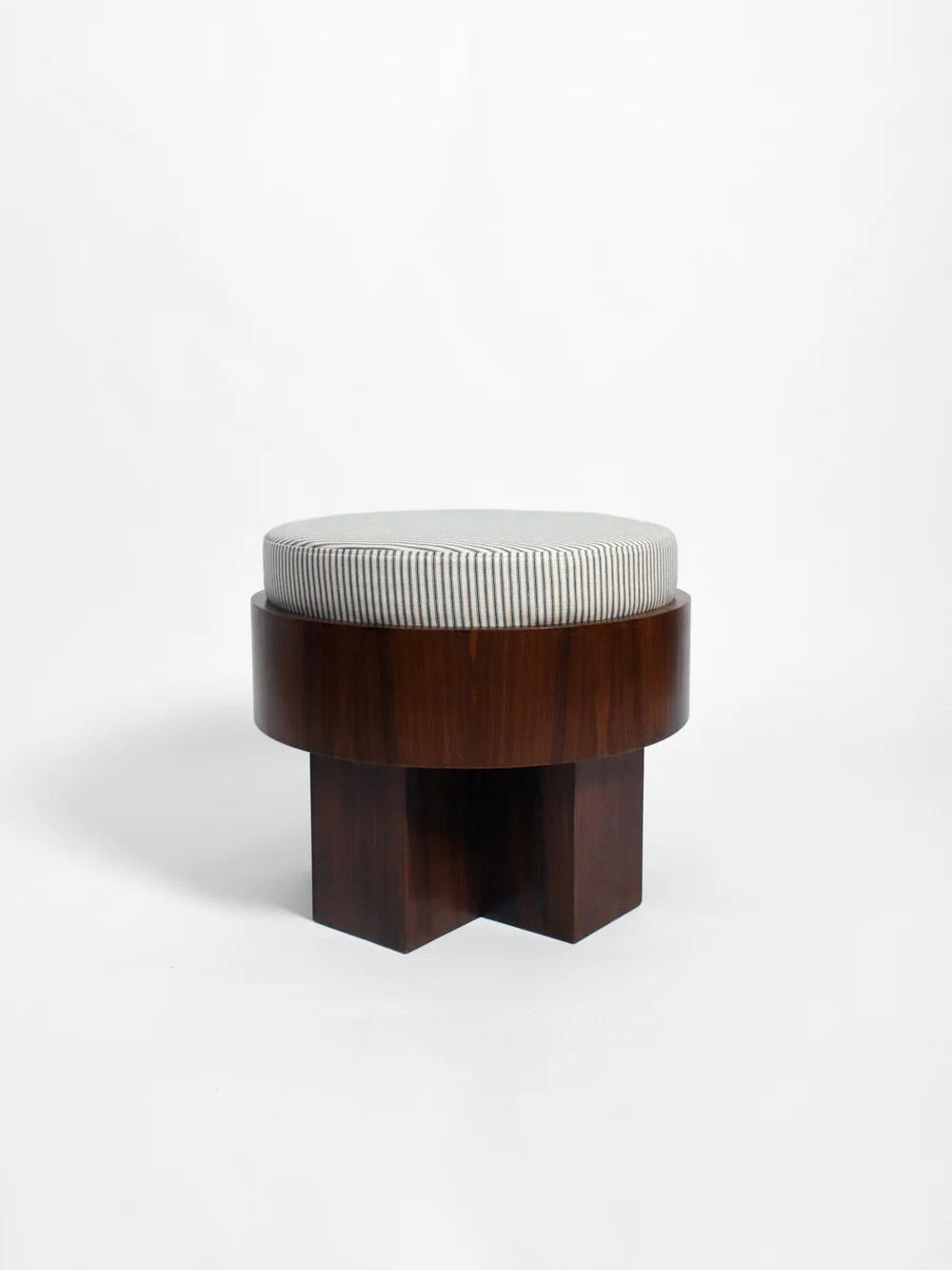 The "Vitruvio" Walnut stool from Barracuda Interiors features a round, cotton striped cushion on its seat. The base is crafted from dark brown wood with a geometric, cross-shaped design, reflecting the elegance for which Barracuda Interiors is renowned. It is set against a plain white background.