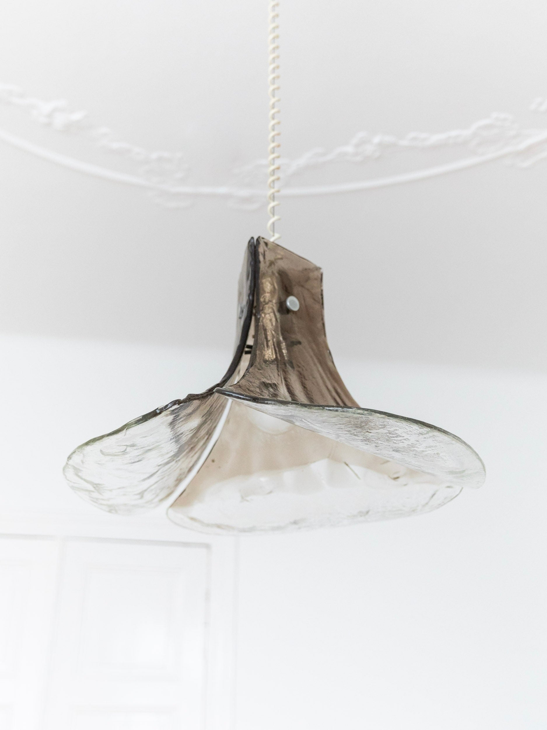 A vintage "LS 185" ceiling lamp by Carlo Nason from Bottega Jacobs features a scalloped, smoked glass shade reminiscent of Muranoglas design. It hangs from a chain against a white ceiling with decorative molding and a faint window outline, echoing the timeless elegance of AV Mazzega.