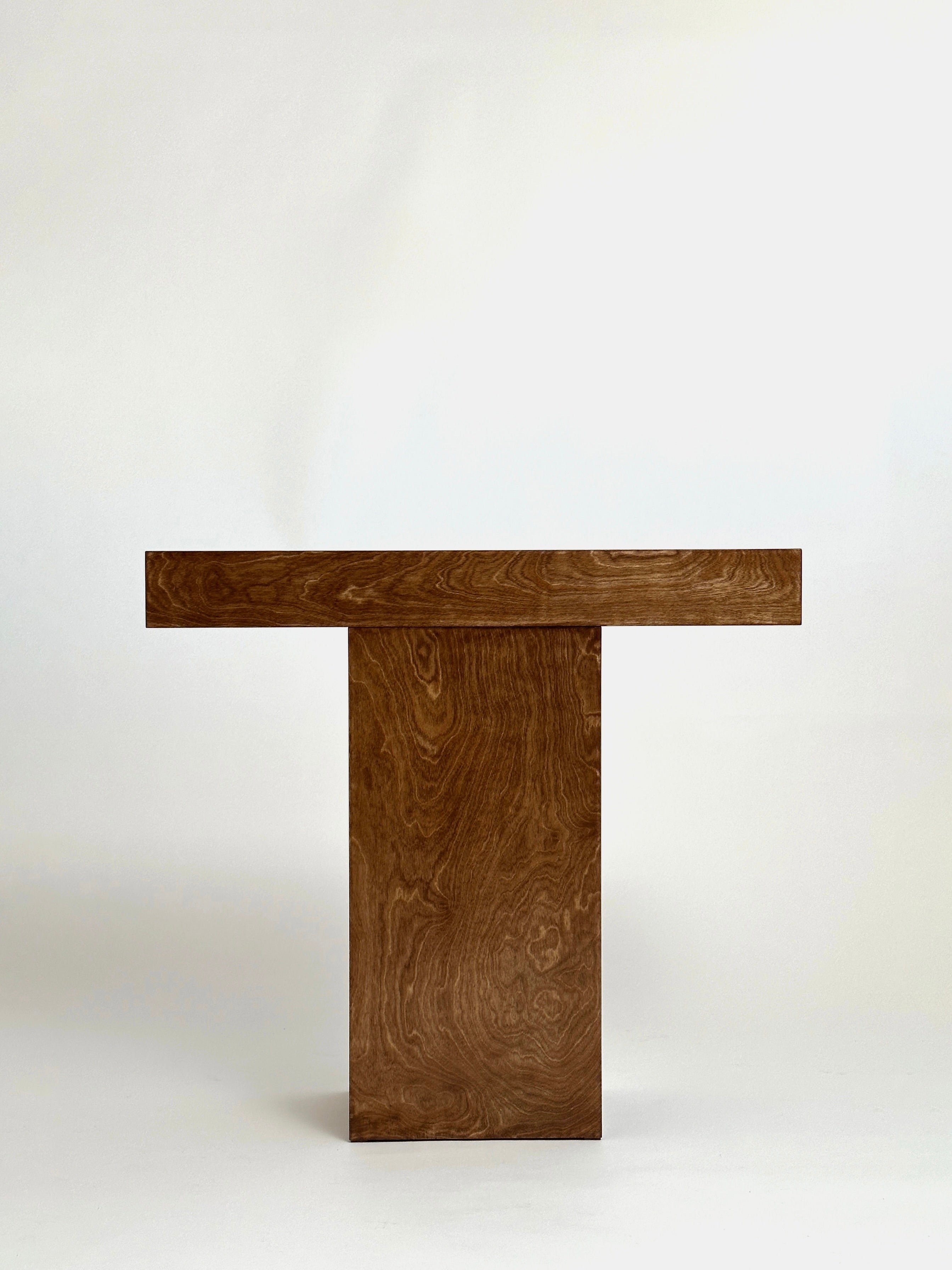 The GOONS Truss Console 02, meticulously crafted by a French studio, showcases a minimalist wooden design with a rectangular top and central support. Set against a plain, light background, it highlights simple yet elegant artistry.