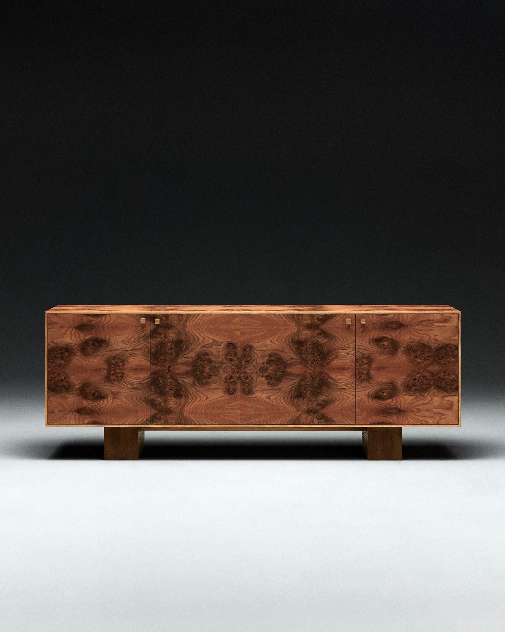 The 'Elm Burl' Sideboard by Axel Wannberg features a symmetrical, intricate wood grain pattern on its doors, four square legs, and small square handles, all set against a dark gradient background.