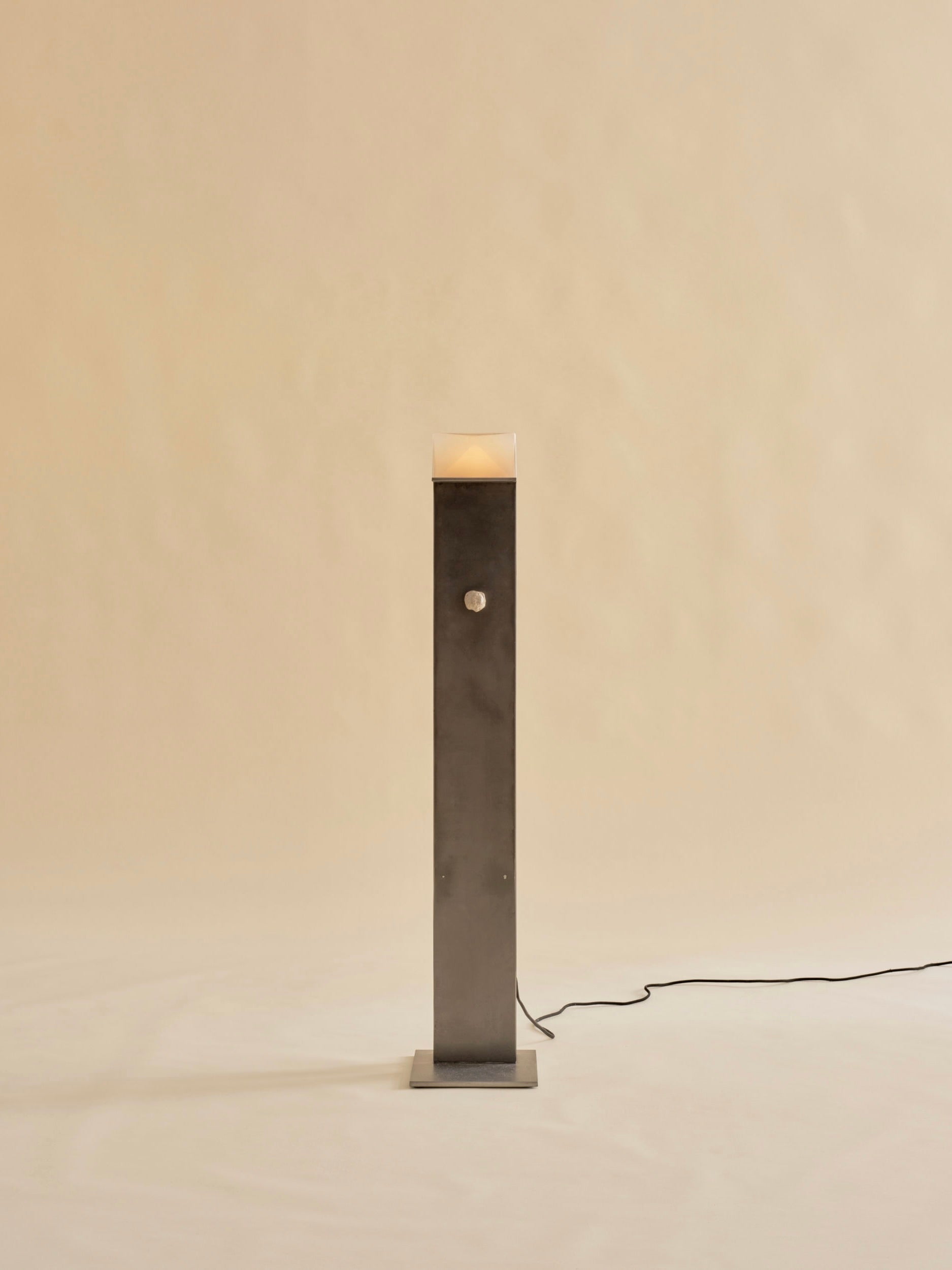 The Perceptions Floor Lamp by Known Work features a tall and slender dark metal design on a simple square base against a beige background, with a handcrafted spherical knob midway and connects to power via a black cord.