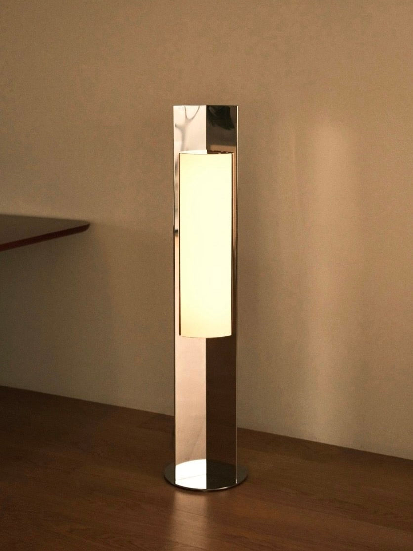 The 'Arrow 120' Floor Lamp by Violaine d'Harcourt is a sleek, modern piece with a tall, rectangular design ideal for contemporary spaces. Its polished steel foot creates a warm glow, beautifully illuminating wooden floors and reflecting off nearby walls.