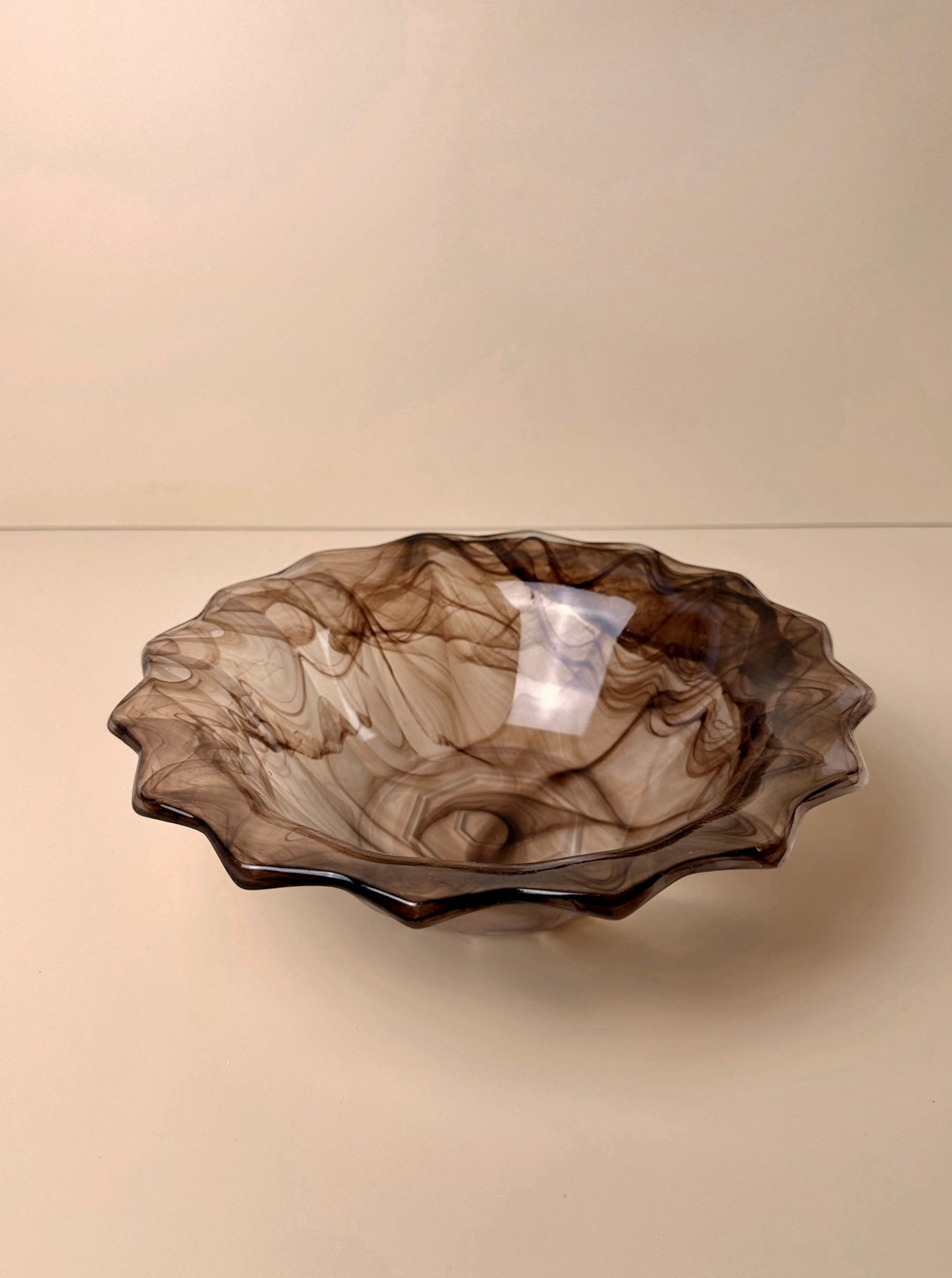 A round, shallow German Art Deco cloud glass bowl from around 1930 with a pointed rim. The Dodo Vintage bowl features a marbled pattern in shades of brown and beige, creating an elegant and artistic appearance. Set against a plain beige background, it makes for a stunning collectible piece.