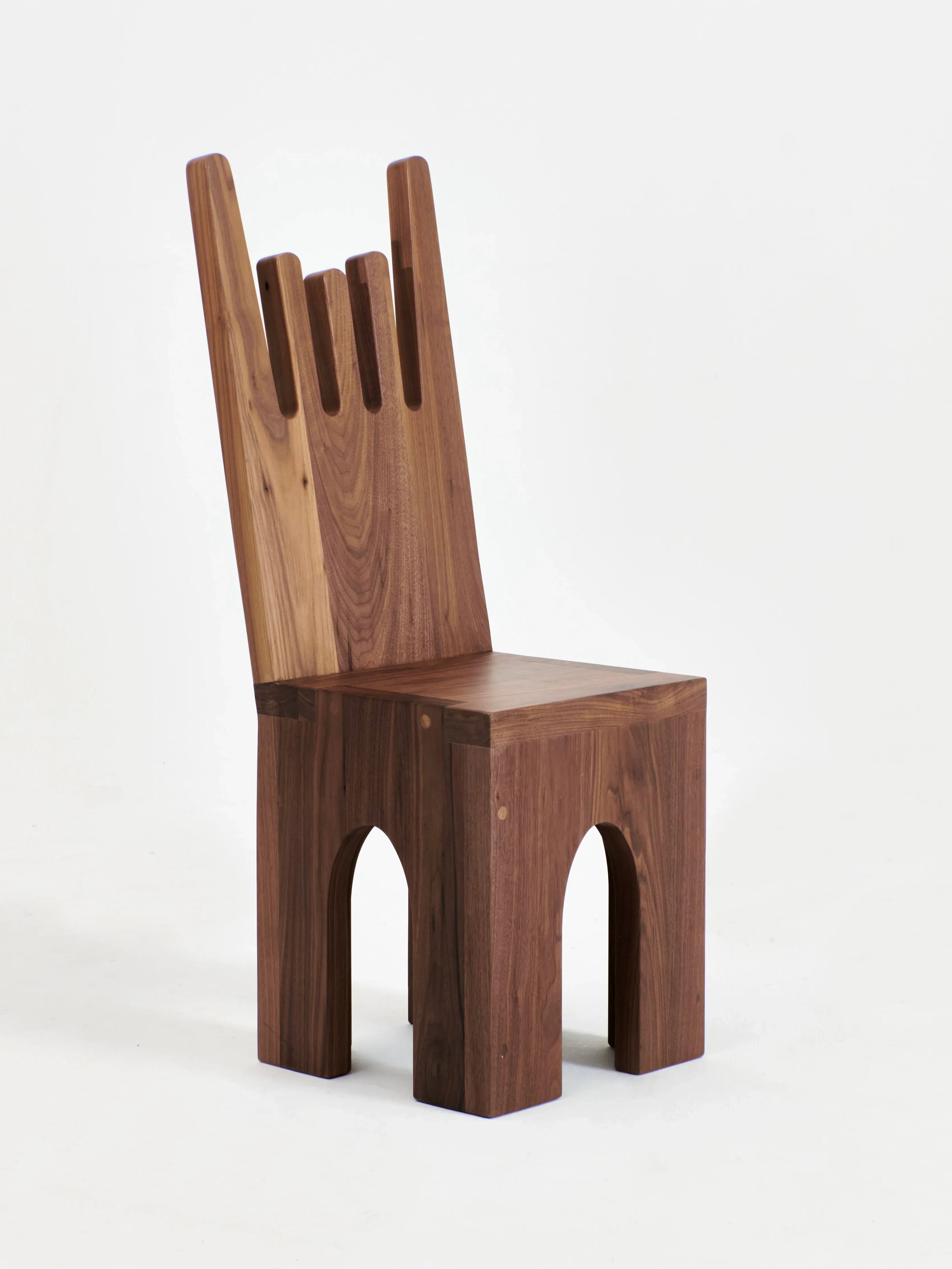 The Portugal Chair No 5 by Project 213A features a unique design with a high, graphic-shaped backrest adorned with three narrow vertical slits. Its arched legs contribute to its distinct and artistic appearance. Crafted from solid walnut, the wood boasts a rich, natural finish.