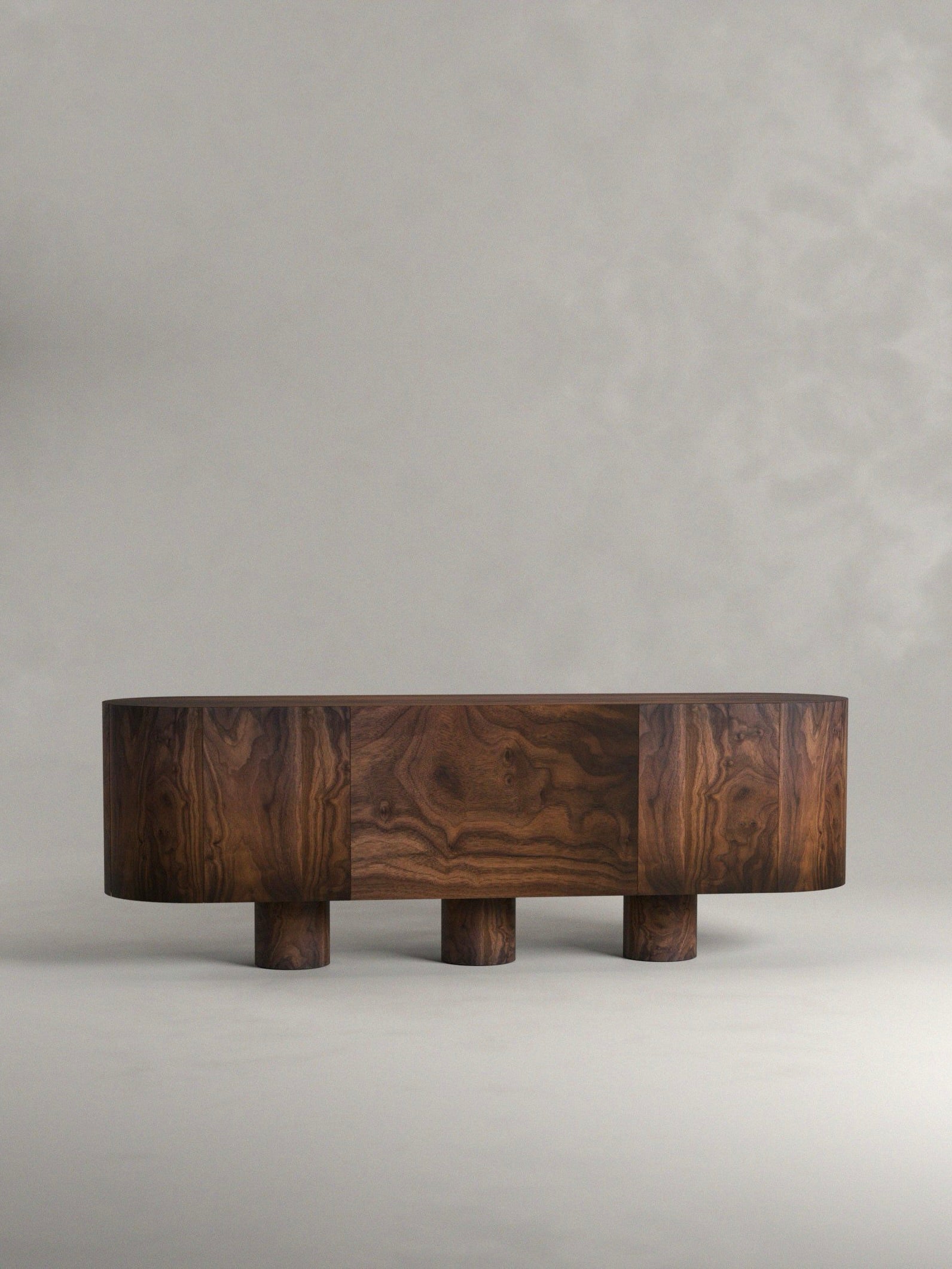 The 'Totem' Sideboard by Siete Studio features a mid-century modern design crafted from solid walnut, displaying rich wood grain and three cylindrical legs, offering totemic charm against a neutral gray background.