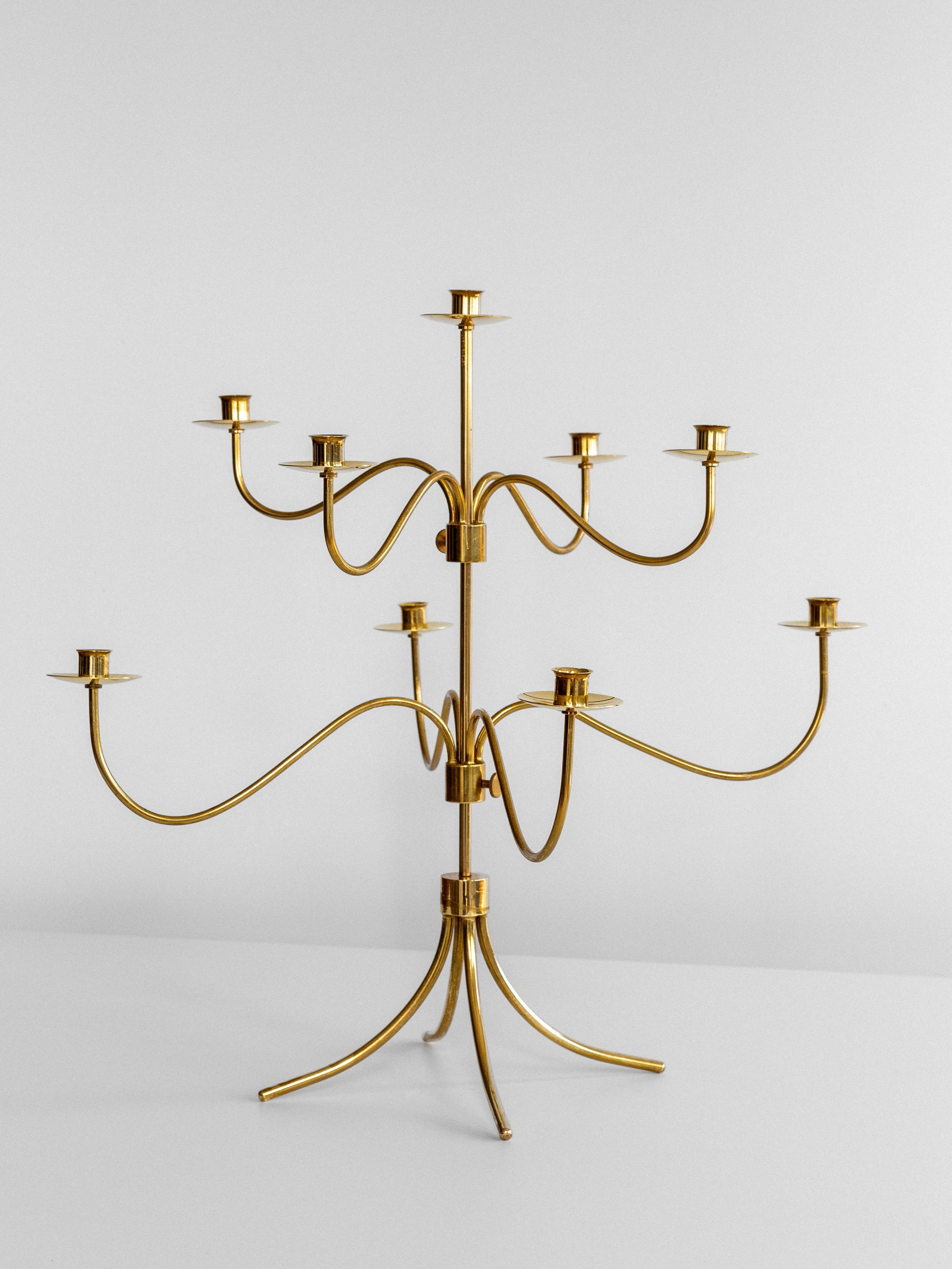 The Large Mid-Century Brass Candelabra by Spigel showcases a modern, minimalist design with multiple curved arms extending from a central stem. Reminiscent of a 1950s brass candelabra, it exudes the timeless elegance characteristic of Josef Frank's designs for Svenskt Tenn. Each arm holds a candle holder at the end, and it is placed on a white surface.