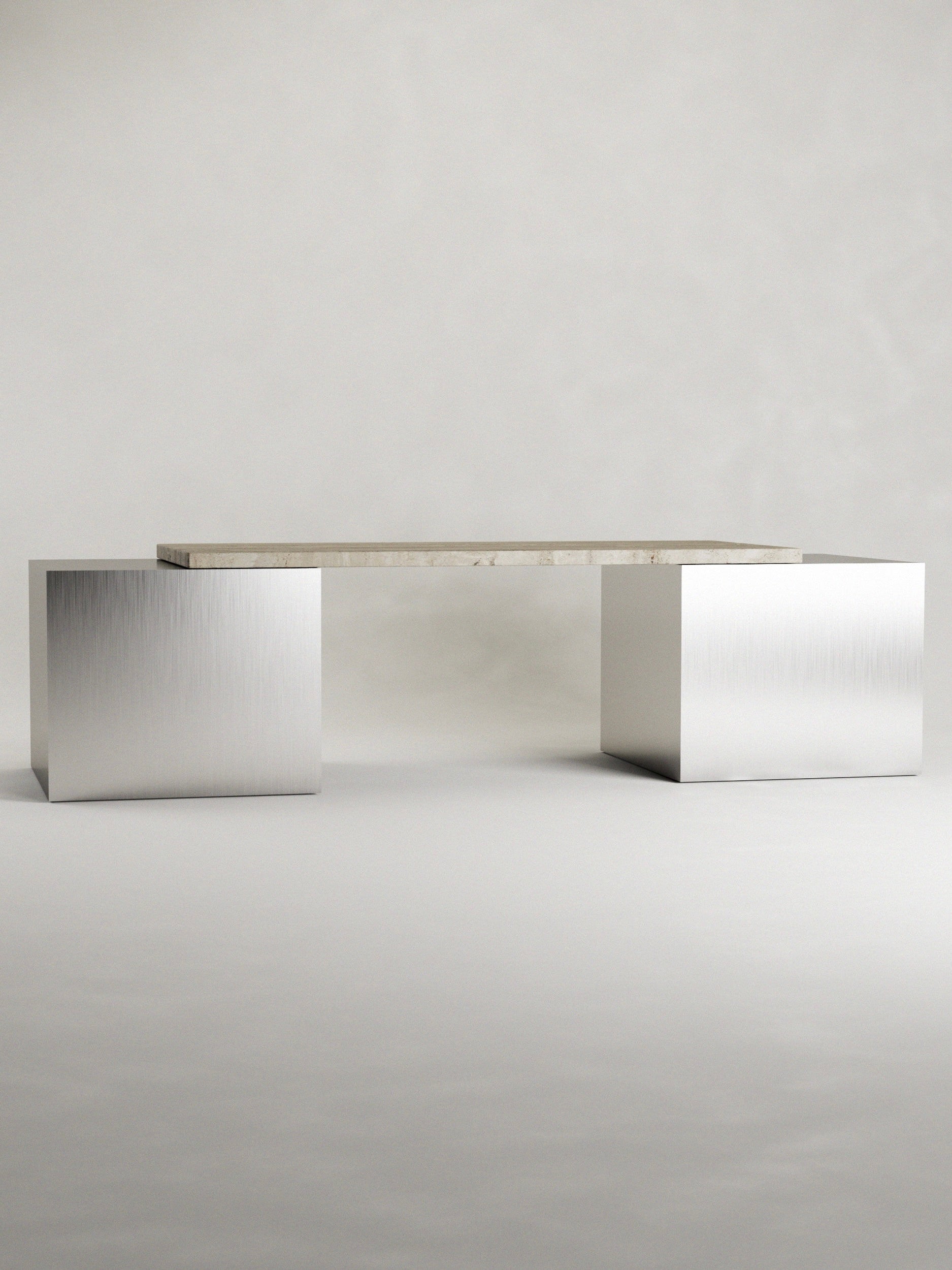 The 'Fragua' Stainless Steel and Travertine Desk by Siete Studio features a travertine top on two metallic cuboid stainless steel bases, all set against a plain, light background.