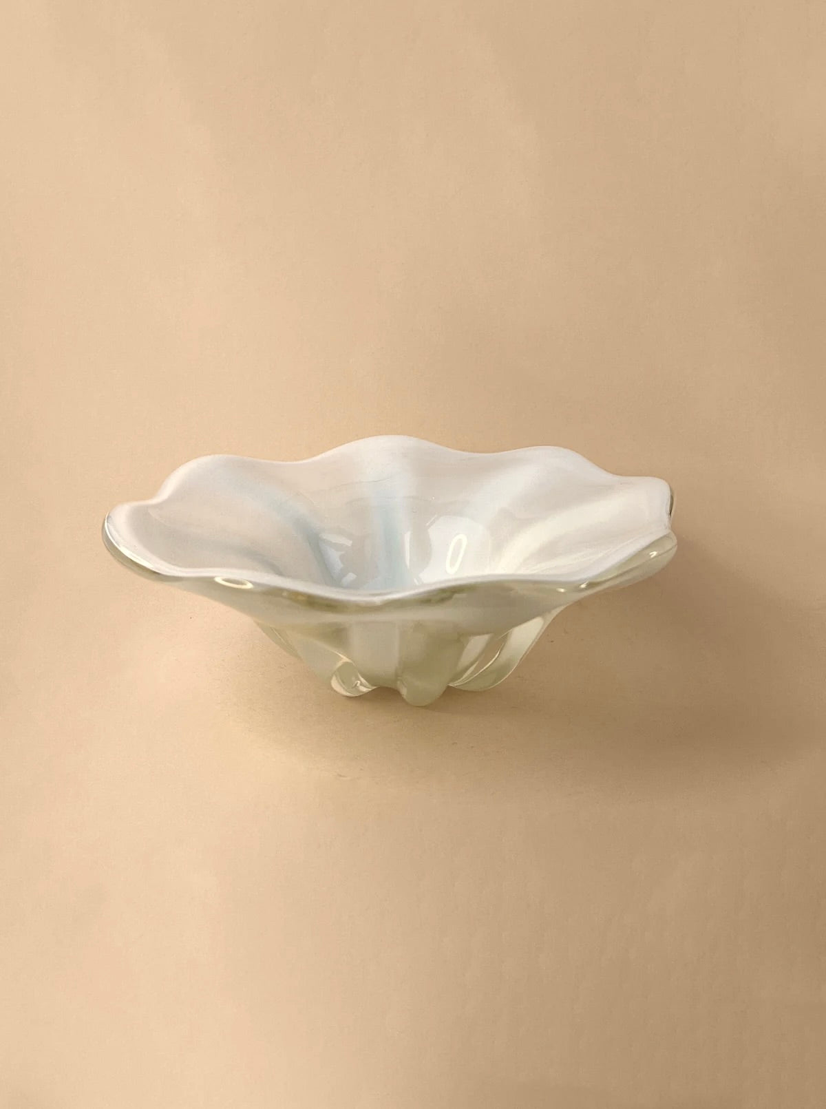 A Mid Century Murano Milky Bowl by Barovier & Toso from Dodo Vintage, with a white, scalloped edge, sits on a beige background. Its curved, petal-like rim and glossy finish give it a delicate and elegant appearance. The bowl's design is positioned centrally, and its shadow faintly visible on the surface beneath it.