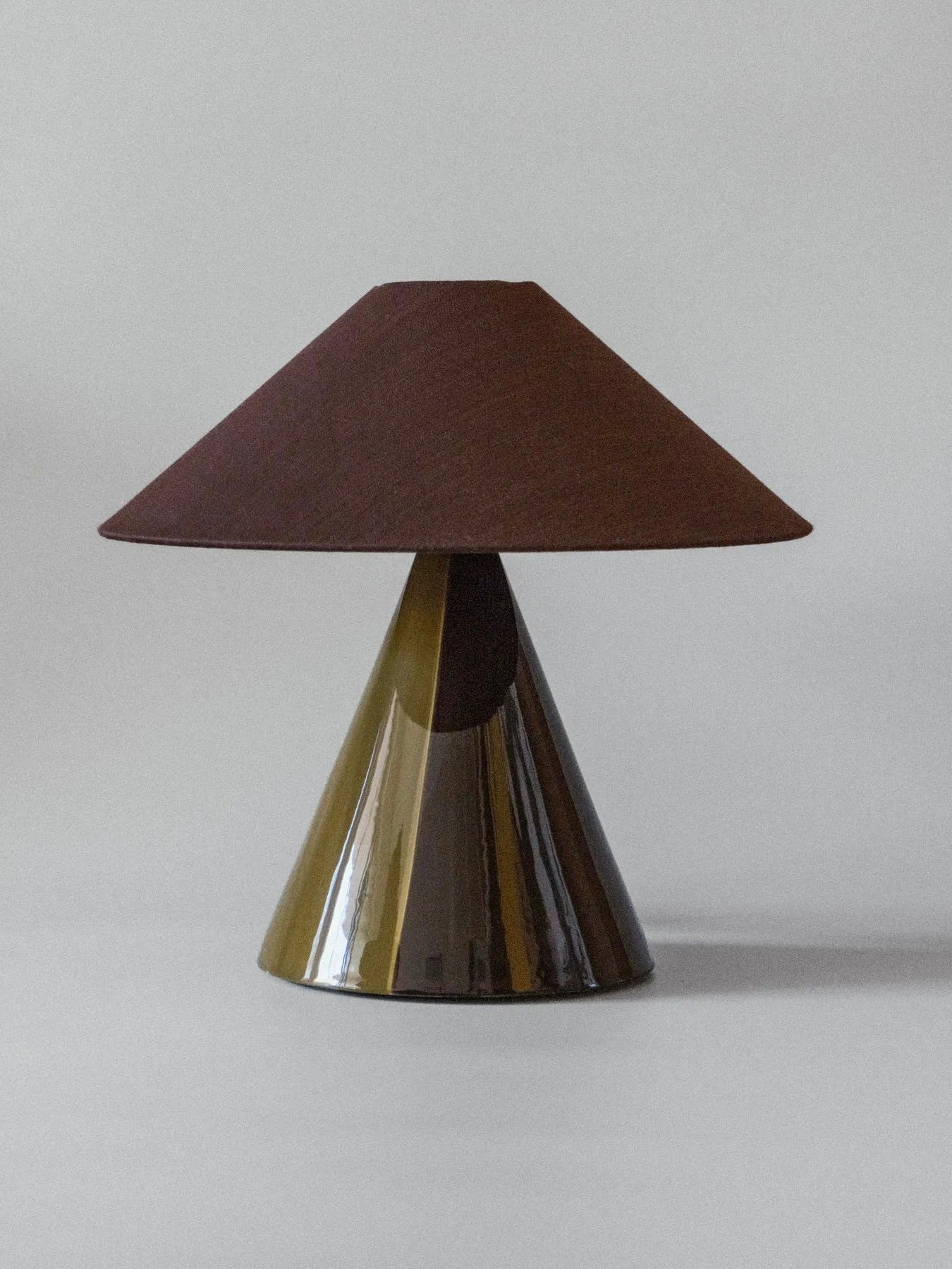 The "Caterina" Dark Brown Table Lamp from mattina moderna features a conical base and wide, dark lampshade with a glossy finish. Its hand-painted design enhances its sleek, contemporary look while adding artistry against a neutral backdrop.