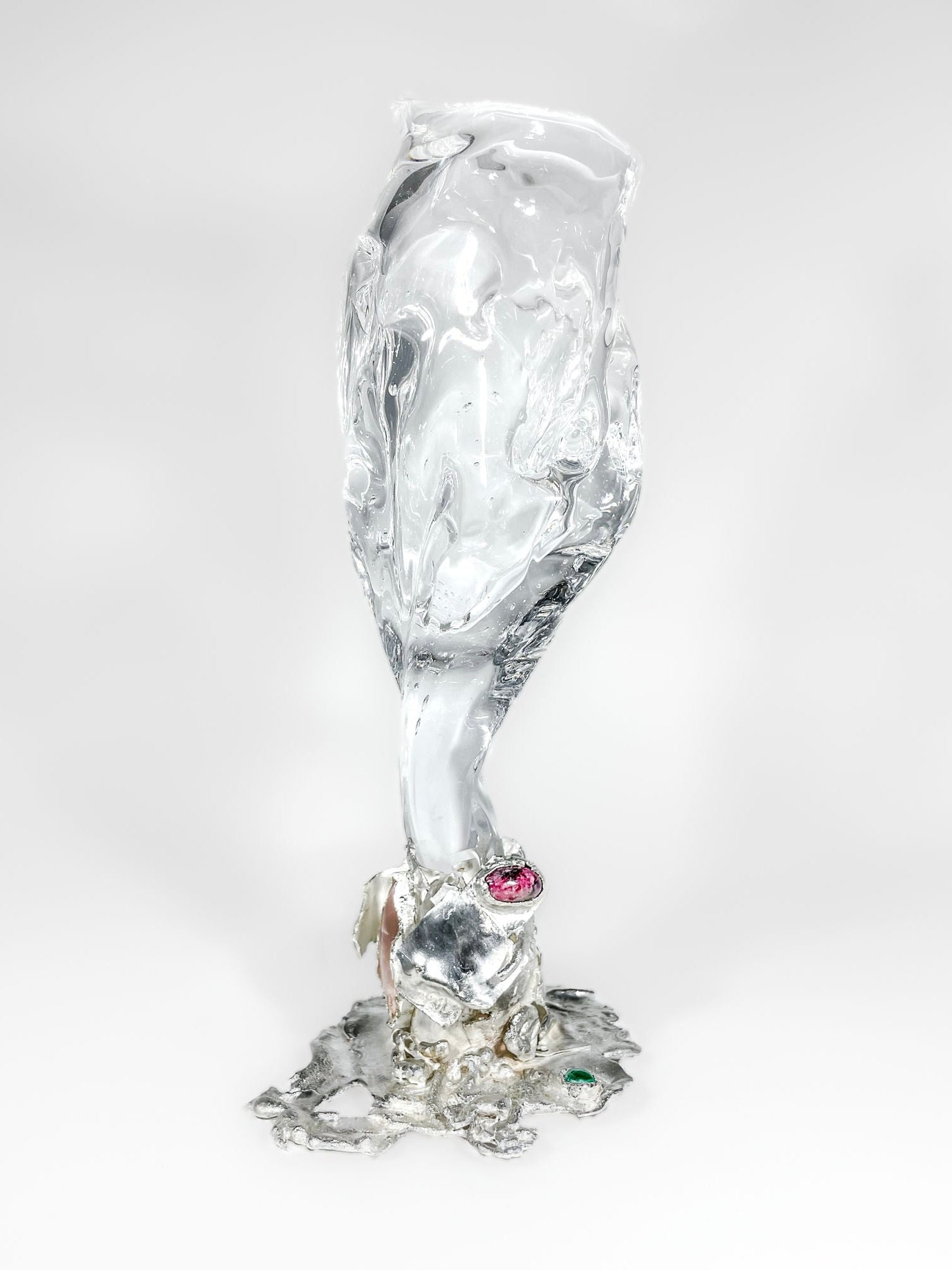Introducing the Jewelled Goblet no. 3 by Lindsey Fontijn from Szkło Studio—a unique sculpture showcasing a hand-blown glass, translucent, twisting, ice-like form emerging from silver stems. The base is adorned with two natural gemstones: one in pink and the other in green. Set against a plain white background, this piece is truly captivating.