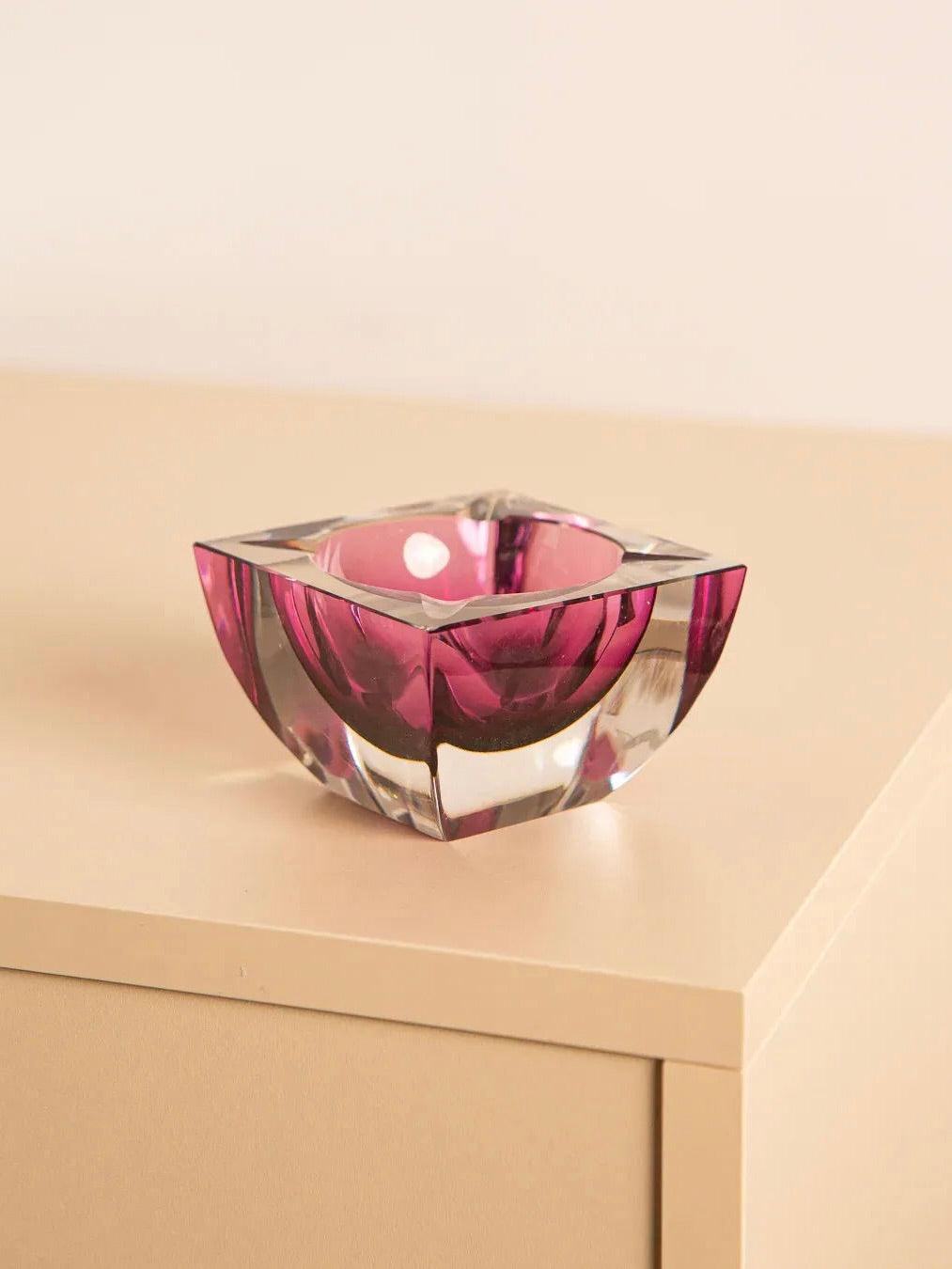 The Square Pink Crystal Ashtray by Val St Lambert from the '80s, available through Treaptyque, rests on a light-colored wooden surface against a neutral background.