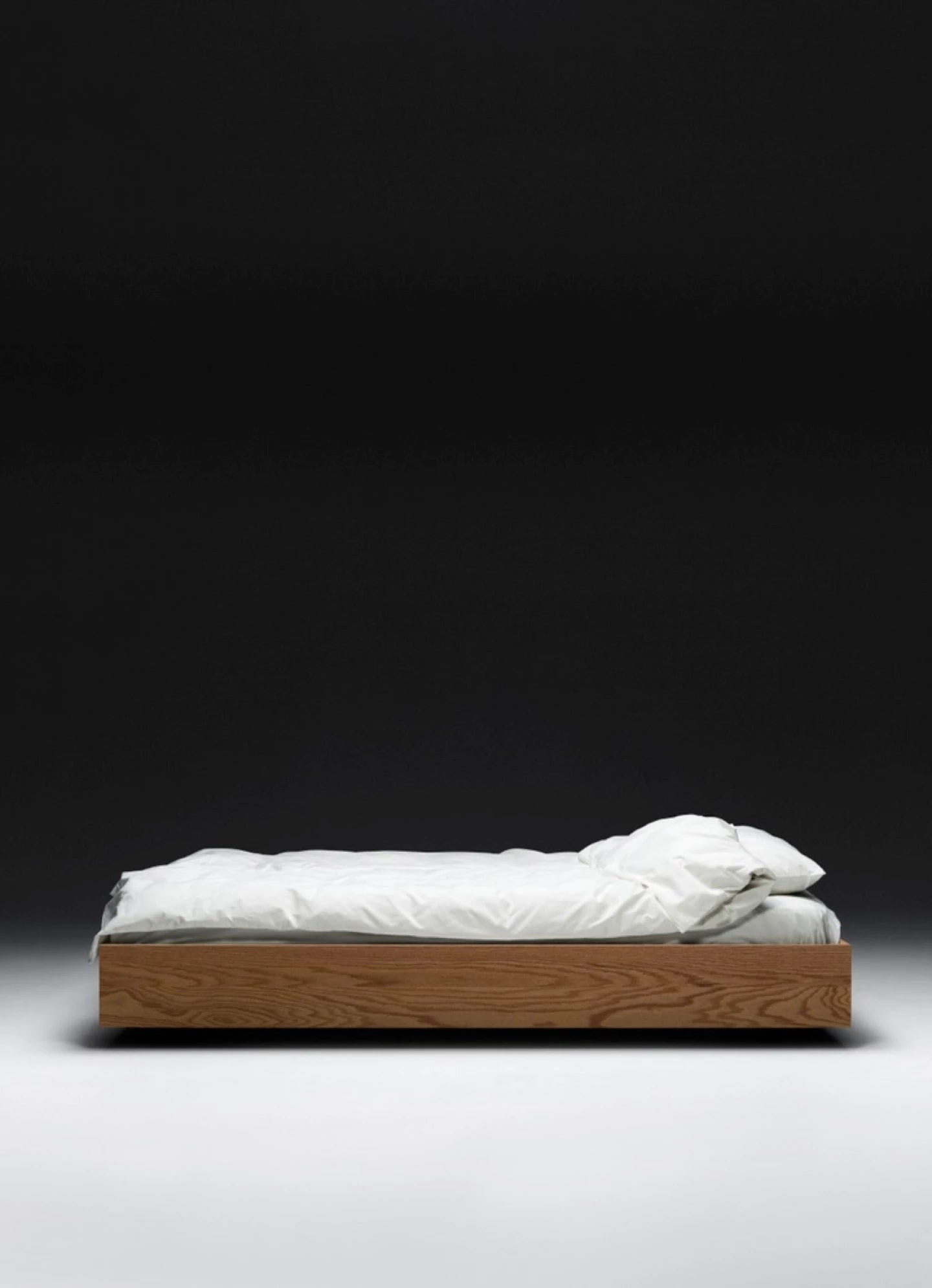 The Floating Bed - Natural by Axel Wannberg features minimalist Red Oak construction with crisp white bedding, set against a dark background to emphasize its modern, artisanal design.