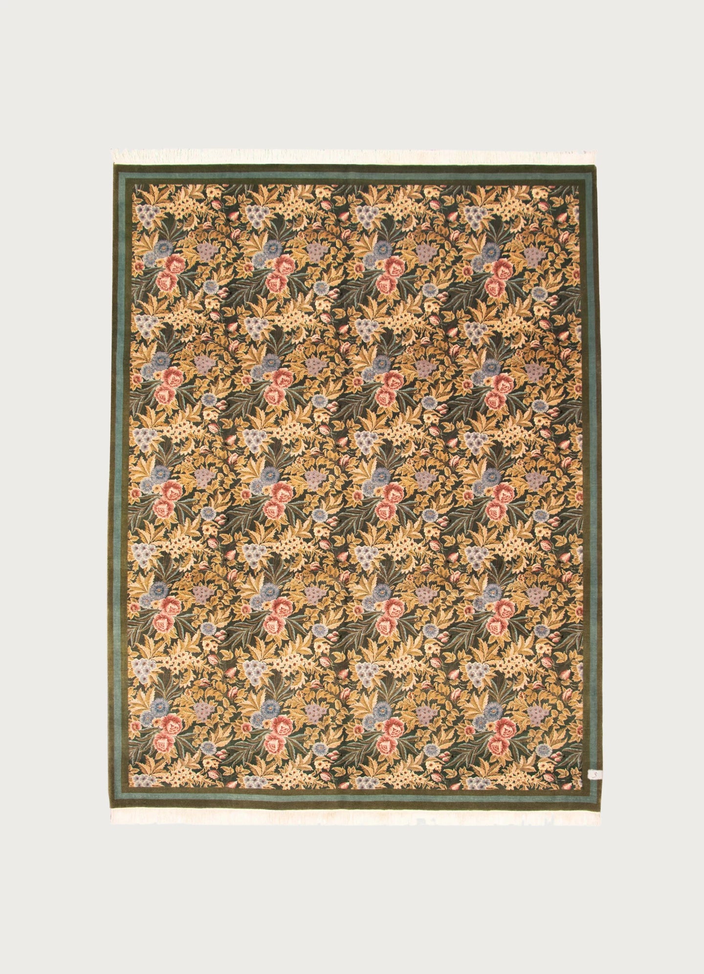 The Morris Rug in Nazm by catalog:three (274 x 369 cm) is a rectangular hand-knotted wool rug with a green border, repeating yellow, red, and blue floral patterns on a dark background, and short white fringes on both ends.