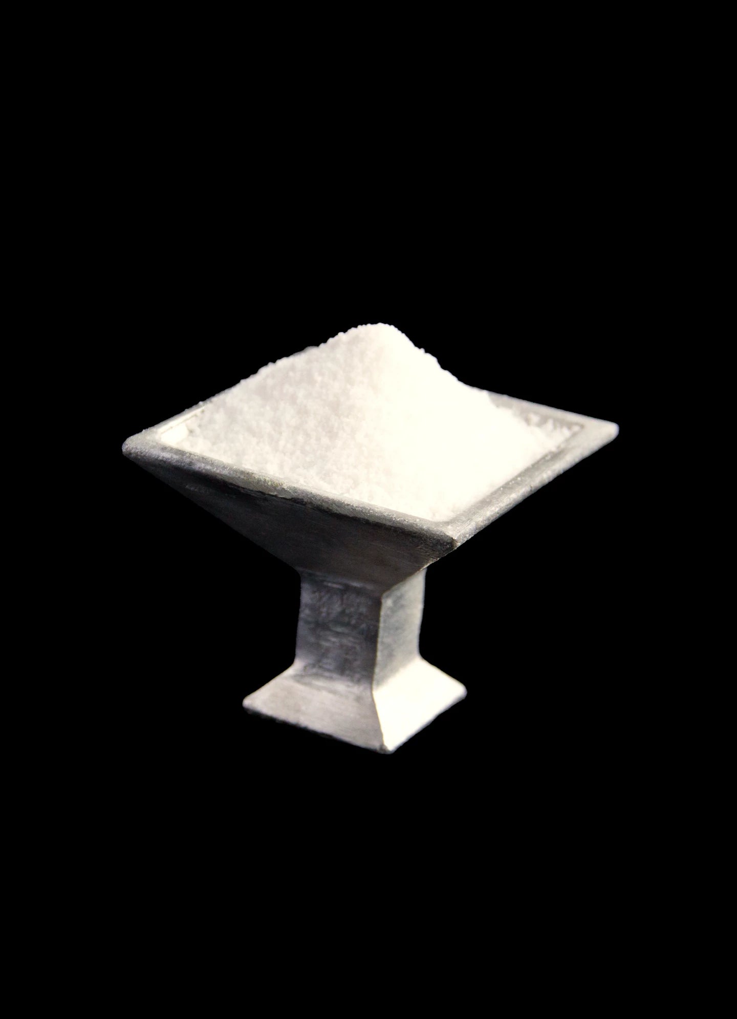 The 'Kare' Serving Coupe by Atelier Barb, crafted from upcycled aluminum, features a heap of white salt set against a black background—a striking showcase of sustainable design.