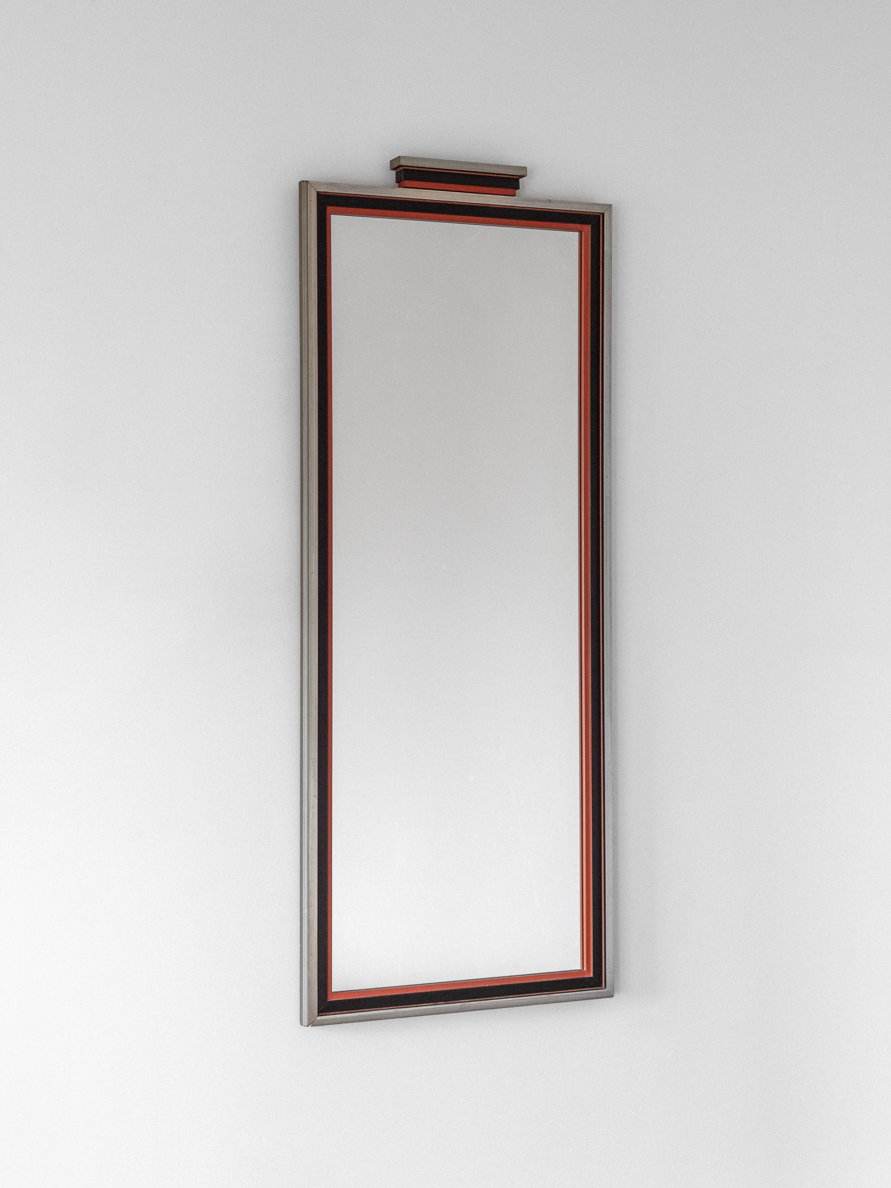 The Spigel Art Deco Mirror from 1930s Sweden, featuring a decorative frame with a subtle red accent, is mounted vertically on a plain white wall.