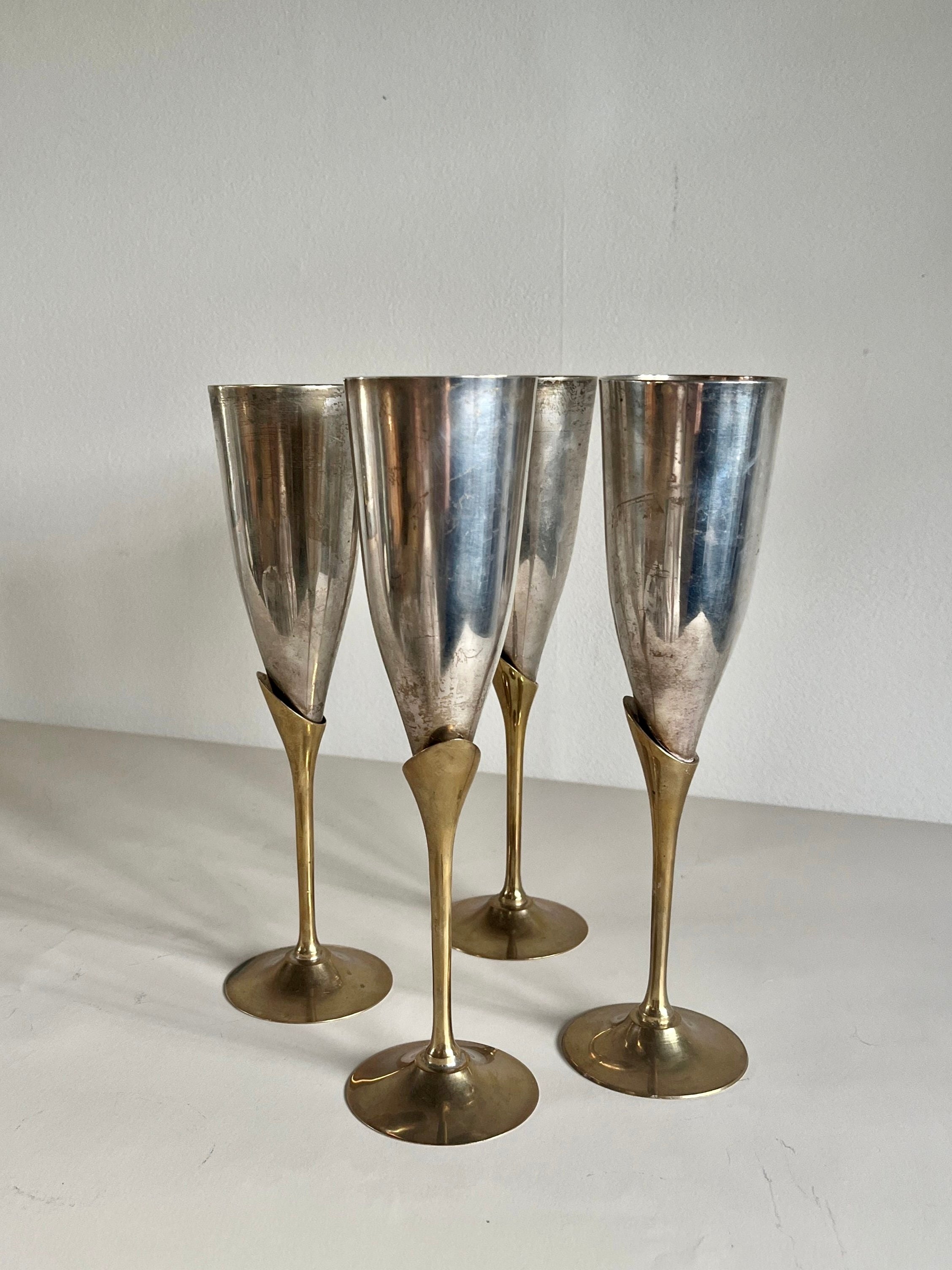 The Maud Vaughan Set of 4 Mid-Century Mixed Metal Flutes features chromed cups and brass-plated stems elegantly arranged on a light surface against a plain backdrop, showcasing tapered cups and slender stems with timeless charm.