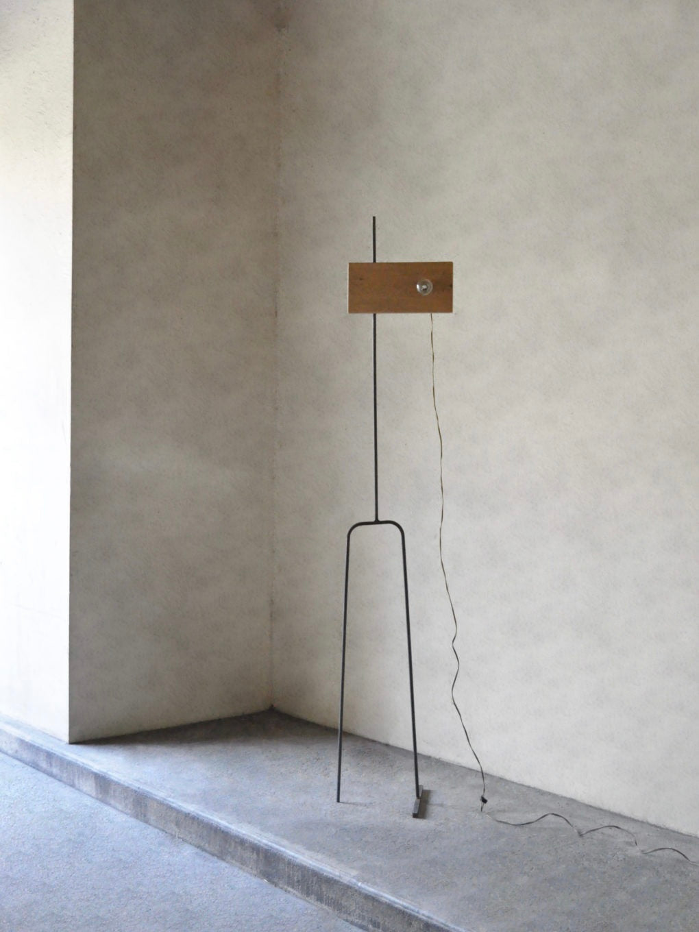 The 'Oiseau' Oak Floor Lamp by Eloi Schultz features a minimalist design with a slim black metal stand, a rectangular oak shade, and an exposed cord that rests on the floor, highlighting its simple, modern aesthetic.