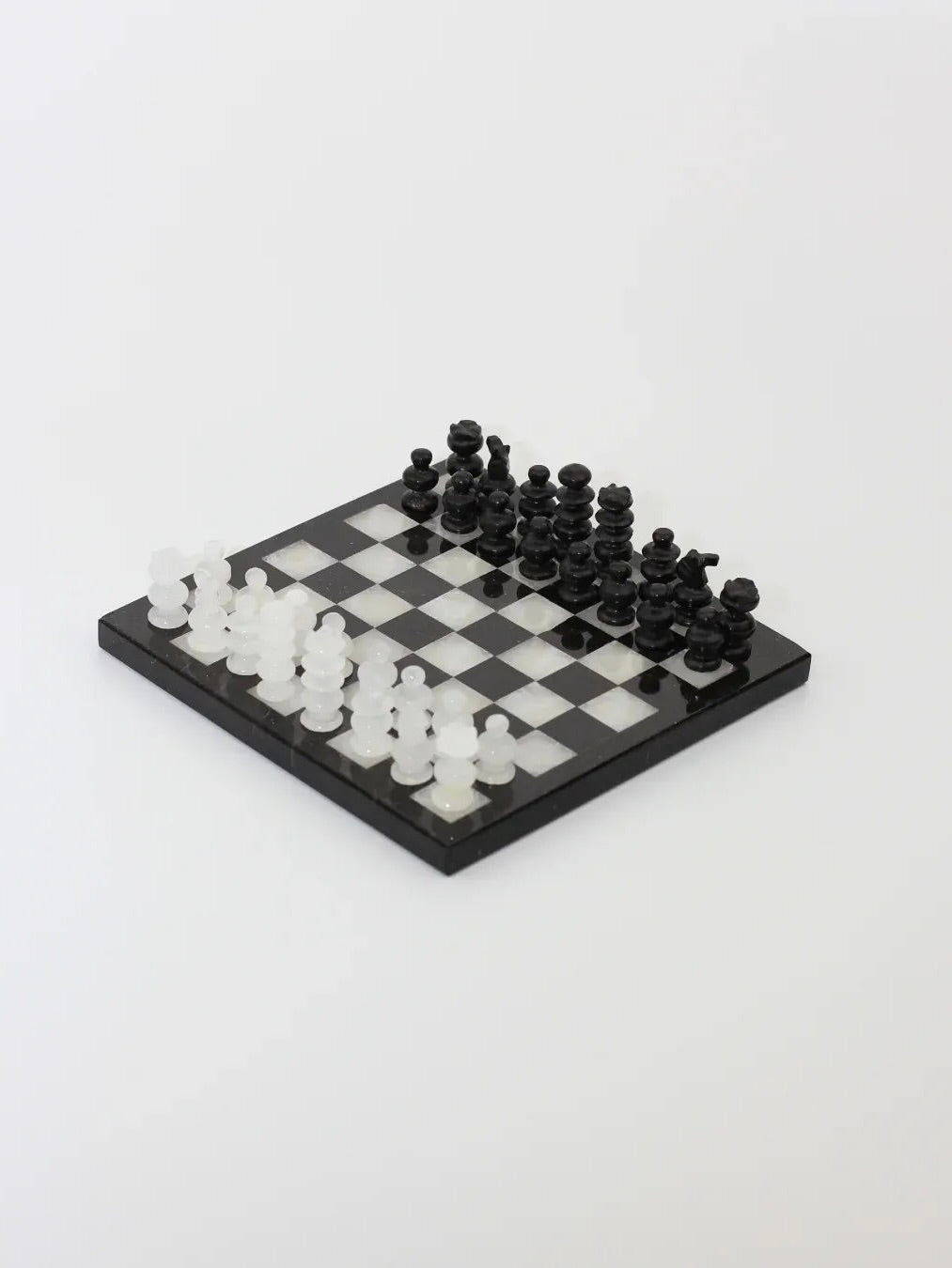 The Handmade Chess Board in onyx from Boga Avante Shop features transparent white and opaque black hand-carved pieces on a classic black and white board. Set up at an angle, the elegant setup is reminiscent of onyx stone.