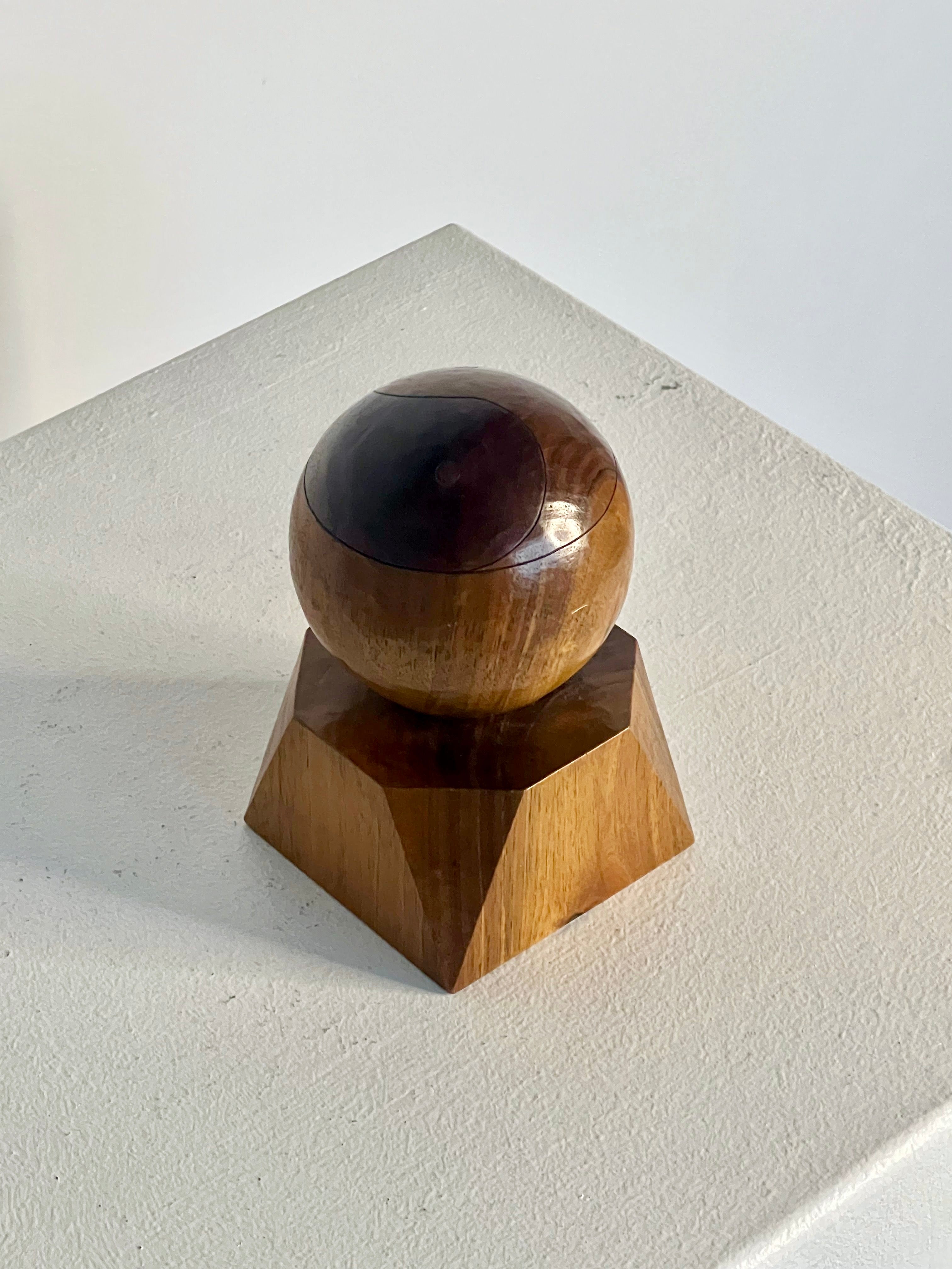 The Yin Yang Orb sculpture by Philippe Gilbert, crafted in 1982 and featured in the acclaimed Porter Studio collection, displays a smooth, polished orb atop a geometric base. Set against a plain white backdrop, the sculpture's rich brown wood highlights its striking grain patterns beautifully.