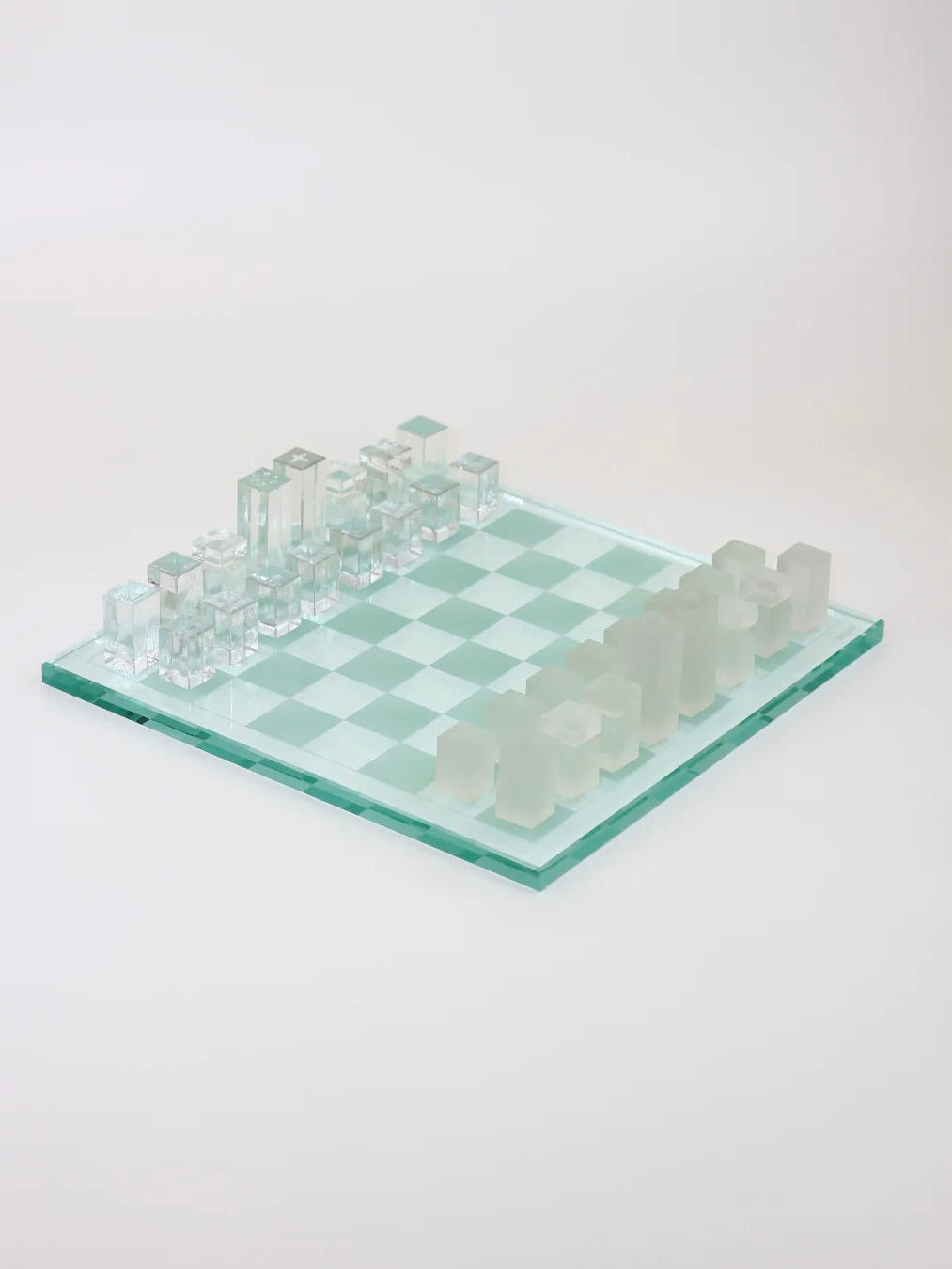 The Boga Avante Shop's Crystal Chess Set features a minimalist design with modern transparent and frosted glass pieces on a green-tinted board, viewed from an angle against a white background.