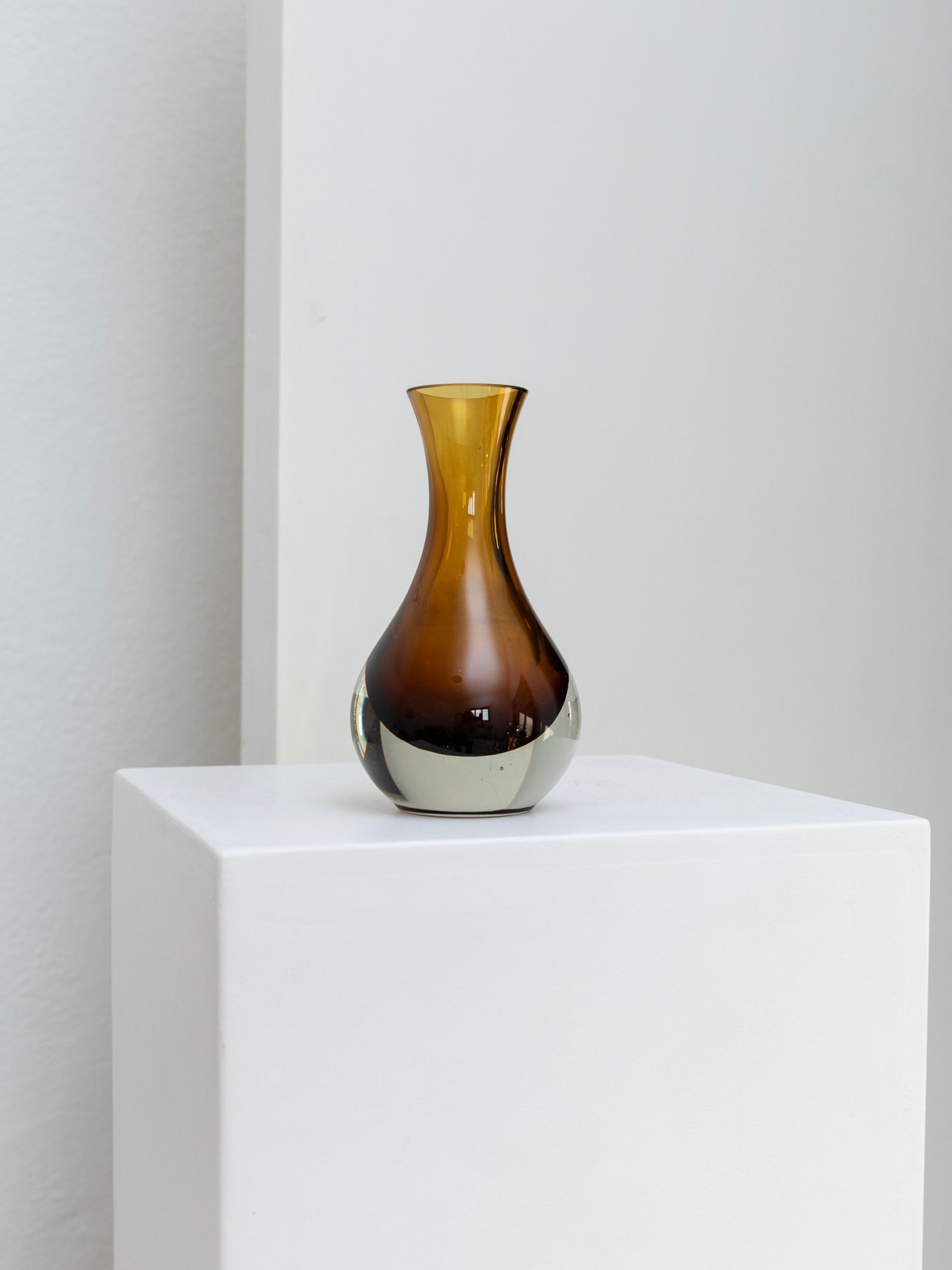 A small, mouth-blown Vintage Glass Vase for Riihimäen Lasi Oy, crafted by Bottega Jacobs, features a narrow neck and round base reminiscent of Tamara Aladin's elegant style. The minimalist design is highlighted by its mustard-yellow color and is showcased on a white pedestal against a light gray background.