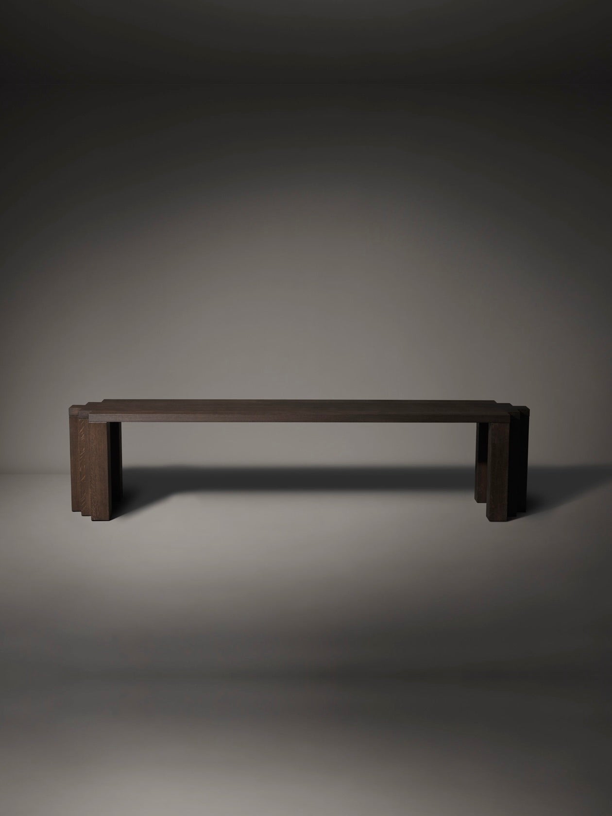 The Mokko Cadence Bench, made from European oak, is set against a softly lit gray background. With its clean lines, rectangular seat, and chunky legs, it exudes modern serenity and customizable elegance for any space.