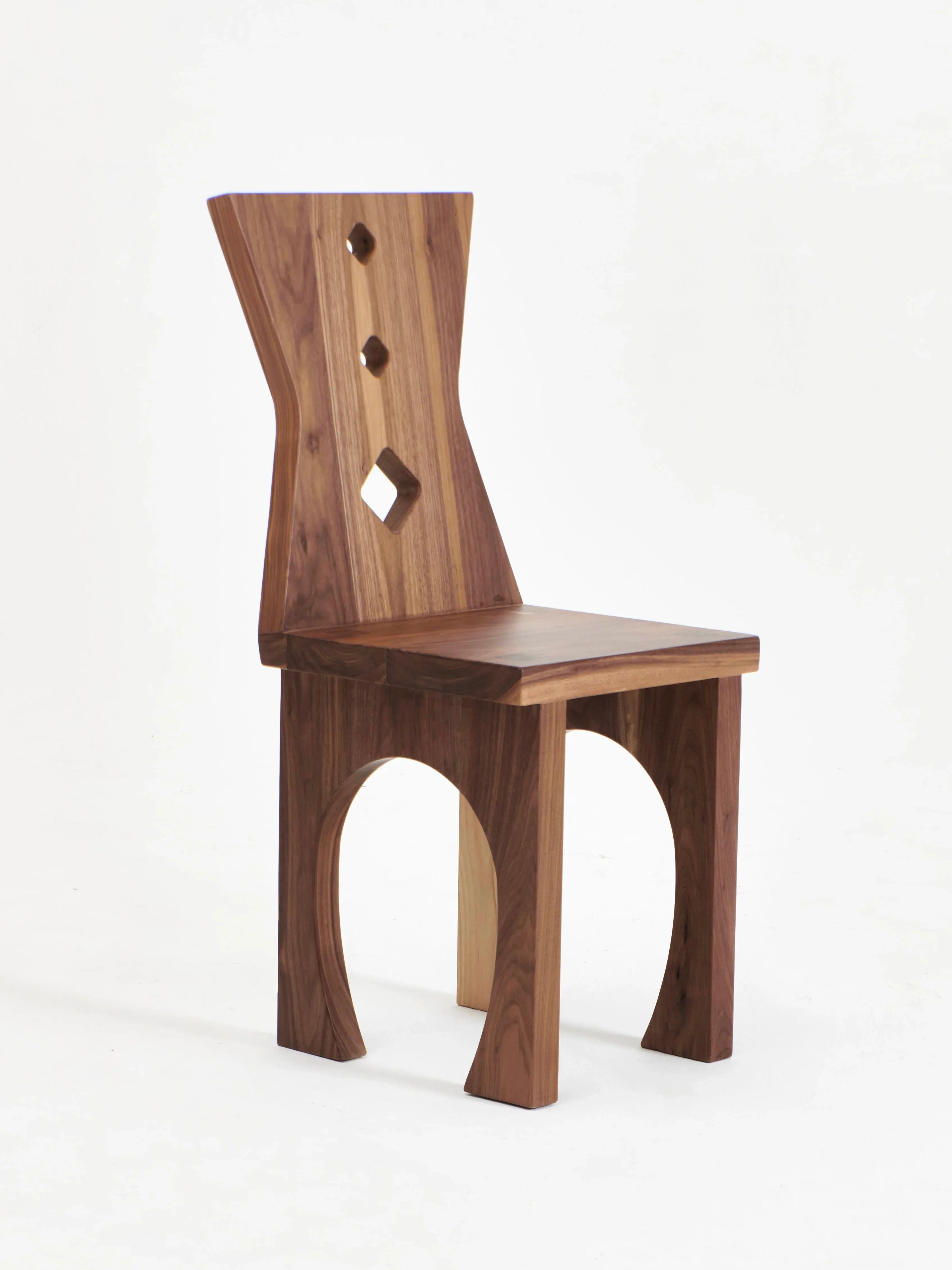 The Portugal Chair No 2 by Project 213A showcases a unique design with a slightly curved backrest adorned with three diamond-shaped cutouts. Its artistically arched legs and solid walnut finish exude elegance. Set against a plain white background, this chair reflects the craftsmanship from Northern Portugal.